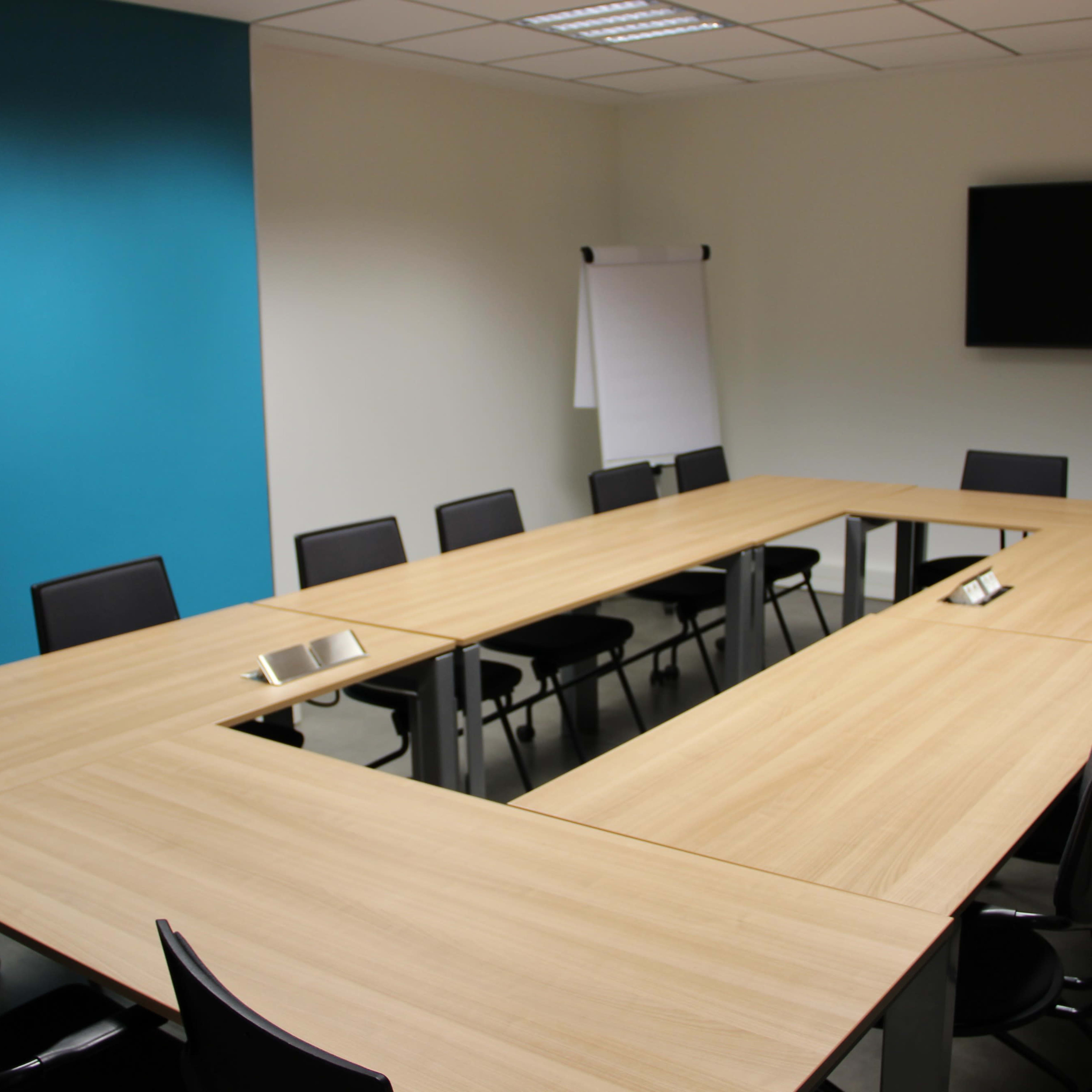 A large conference room features a rectangular table surrounded by chairs, with a presentation screen and a flip chart against the walls.