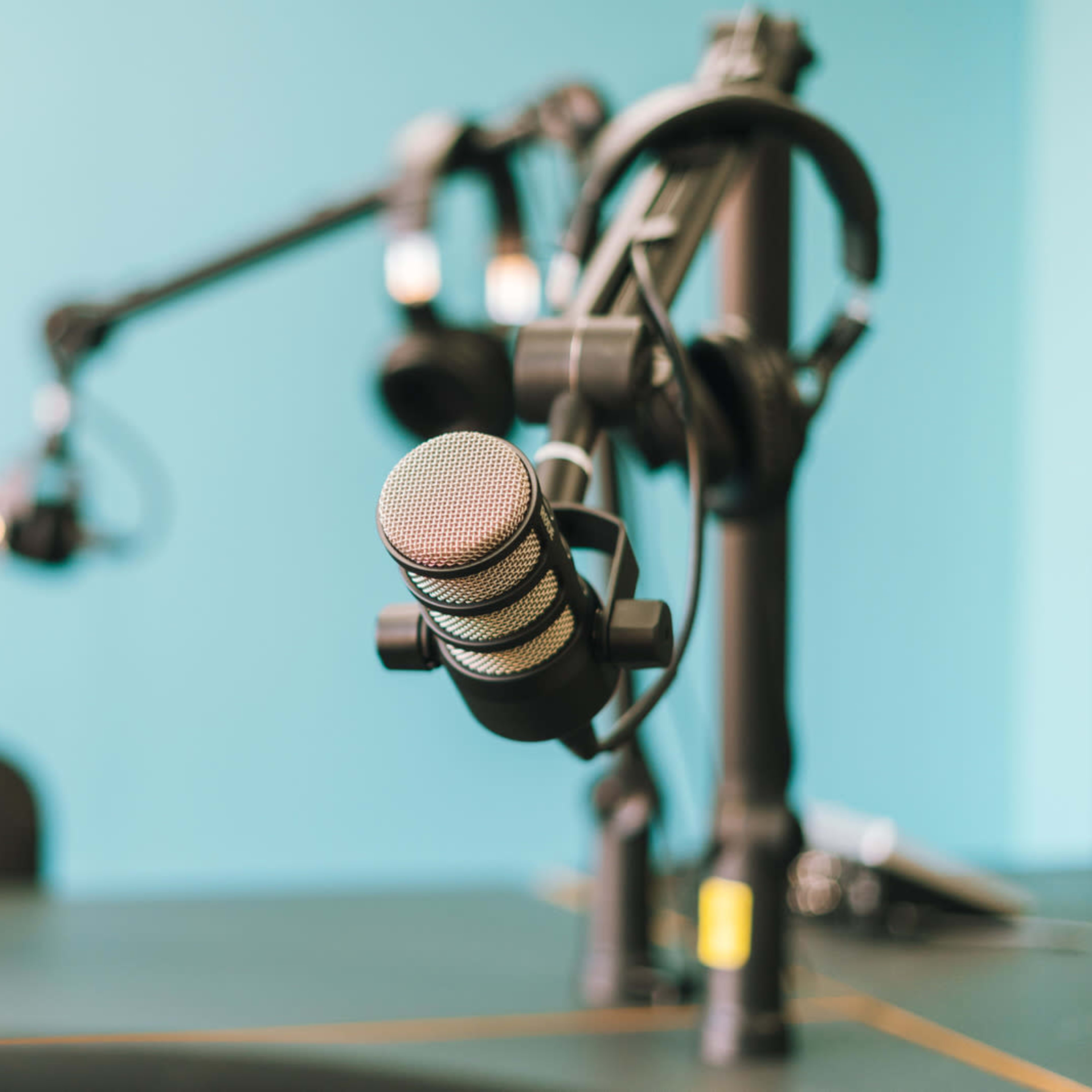 A close-up of a microphone on a stand in a studio with a turquoise wall in the background.