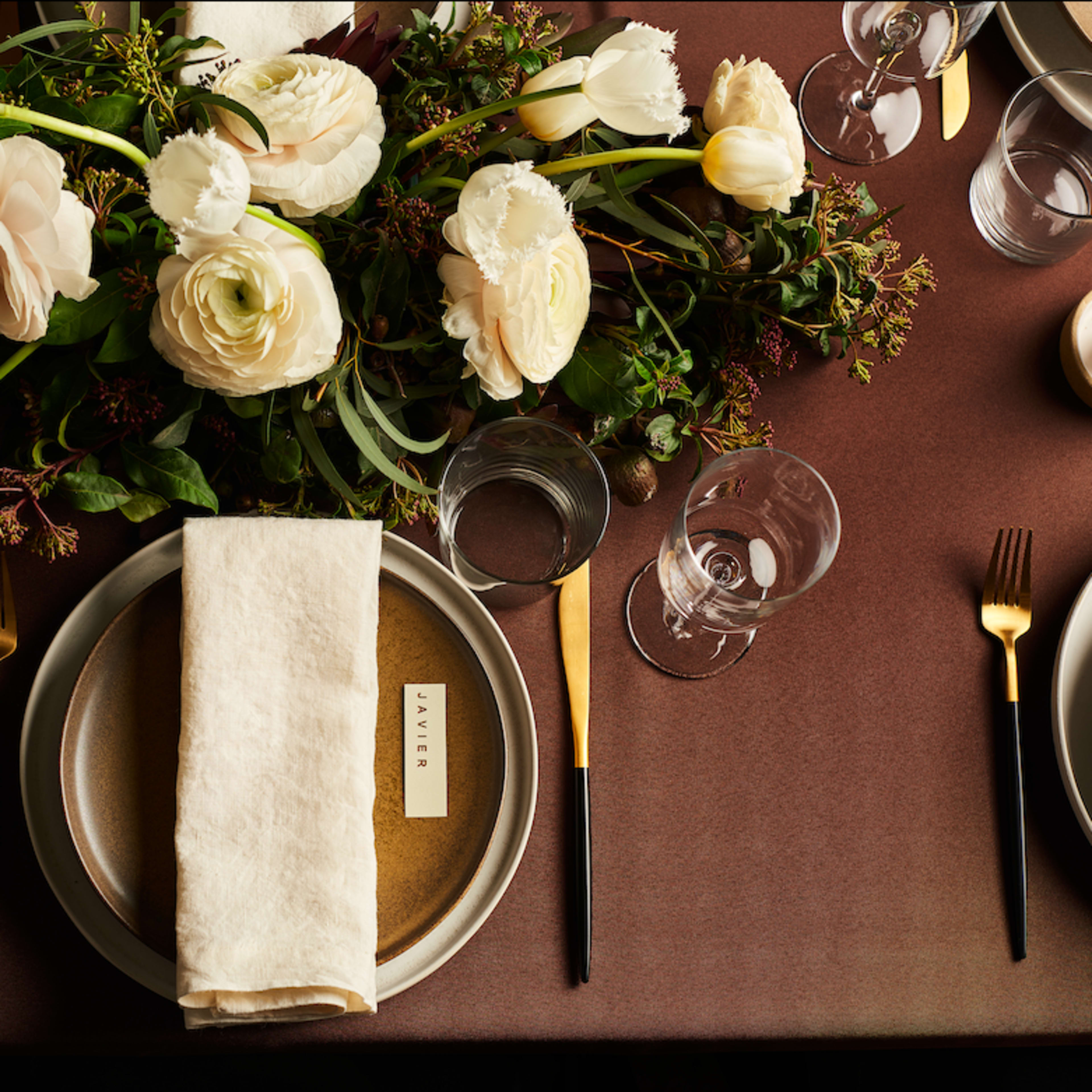 A well-set dining table features elegant plates, glassware, and a floral centerpiece with white flowers and greenery.