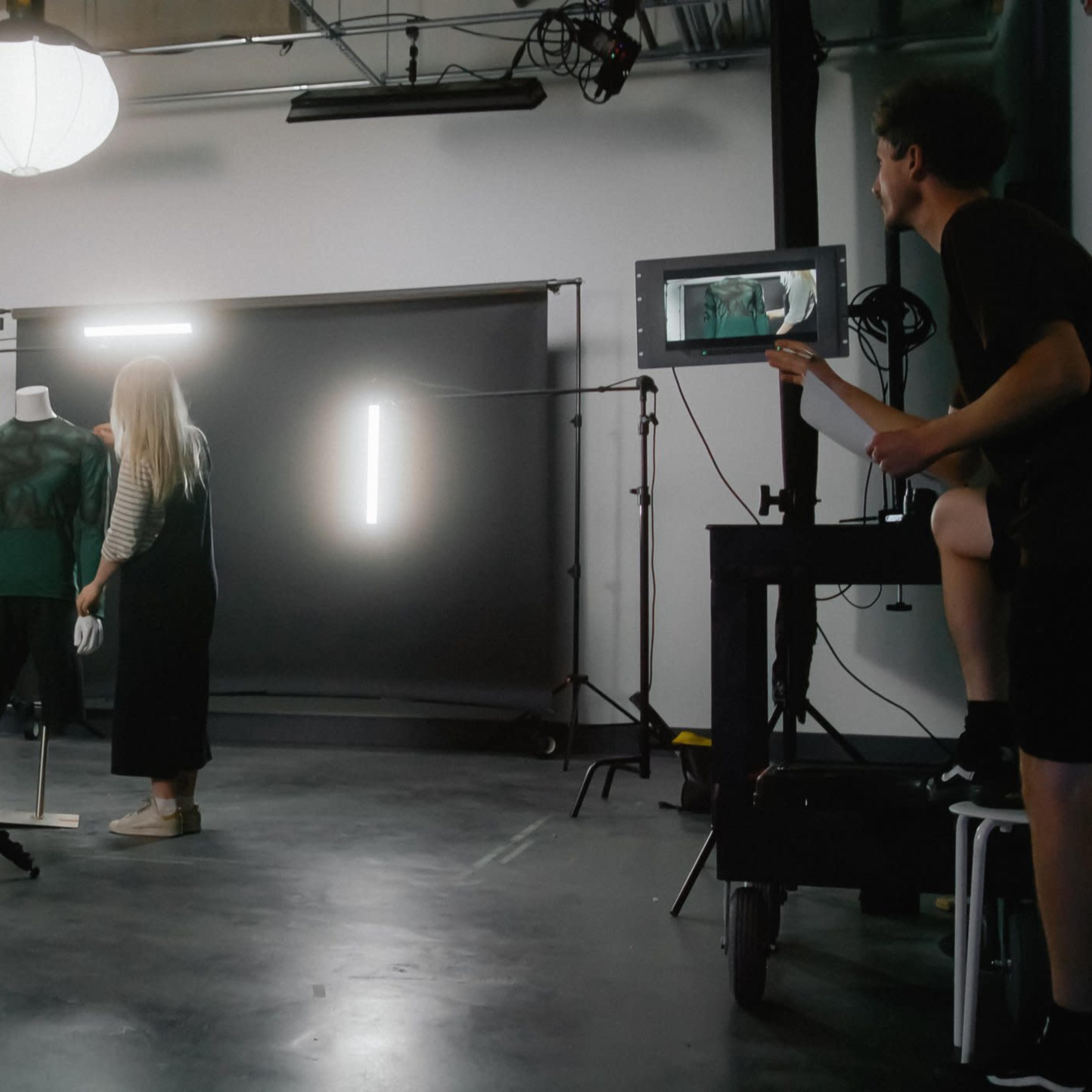 A film crew is setting up a video shoot in a studio with a mannequin and a backdrop.