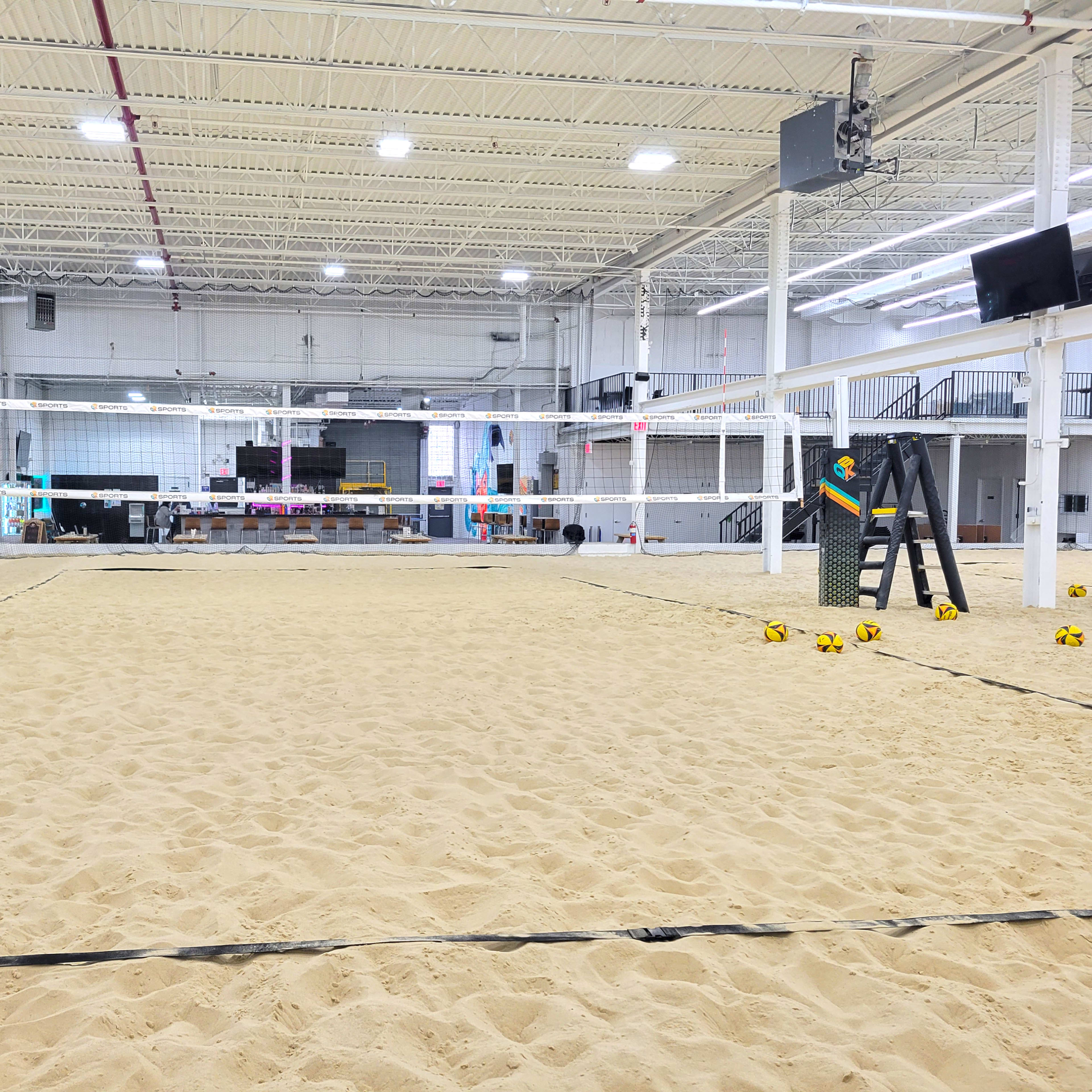 A large indoor sand volleyball court with multiple nets and surrounding seating areas.