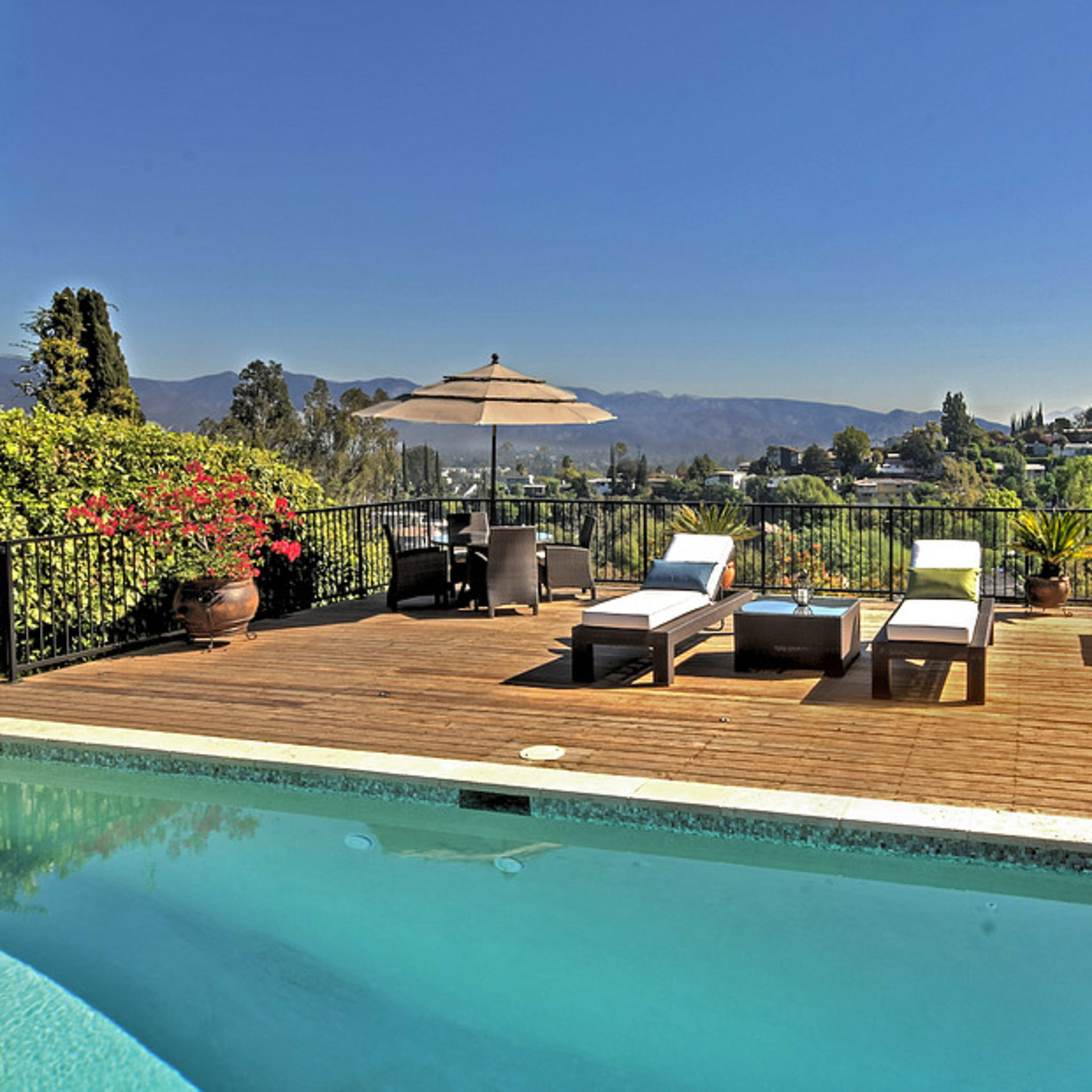 A swimming pool is situated on a wooden deck surrounded by lush greenery and a view of distant mountains.