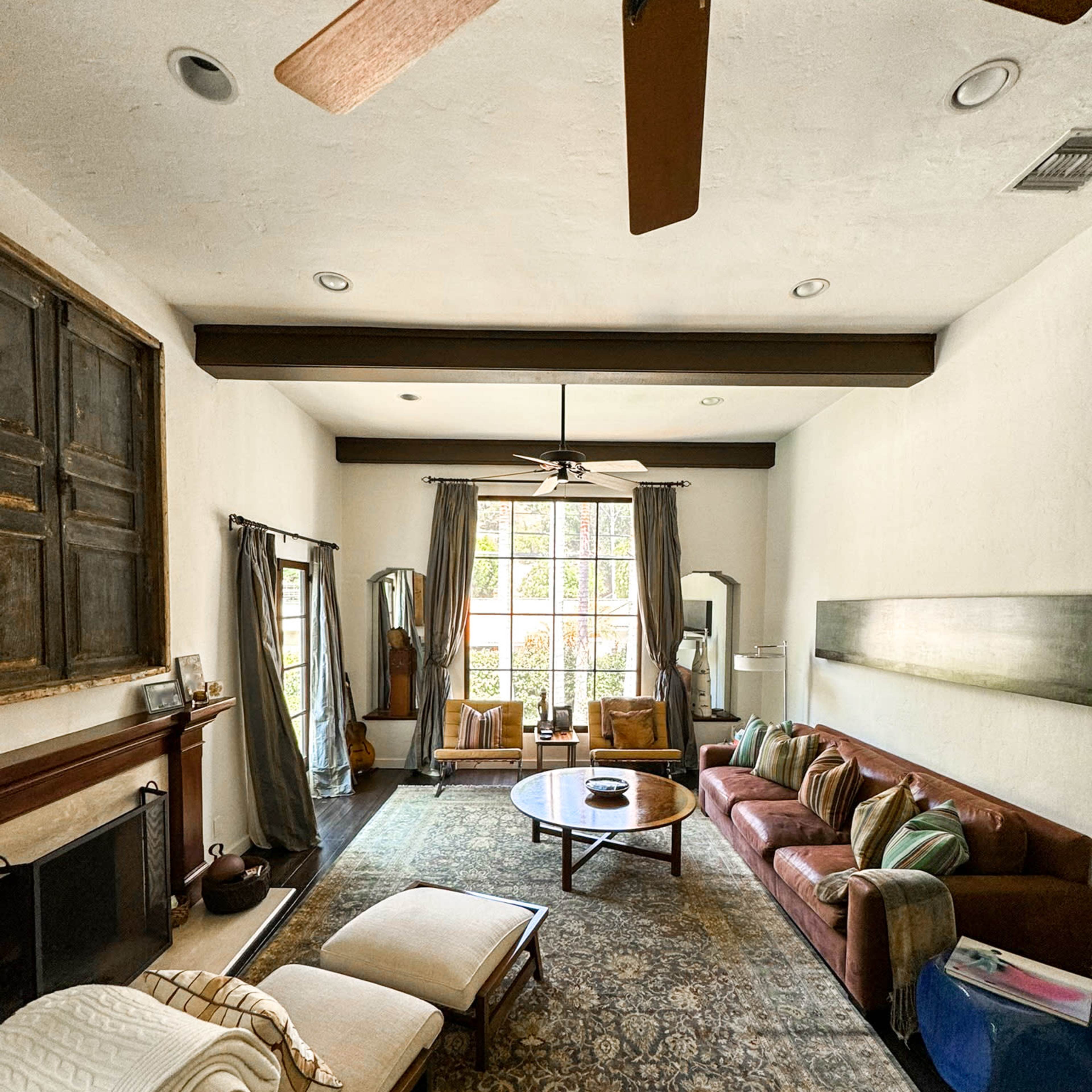 The living room features a large window, a brown couch, a wooden coffee table, and two lounge chairs, with a ceiling fan overhead.