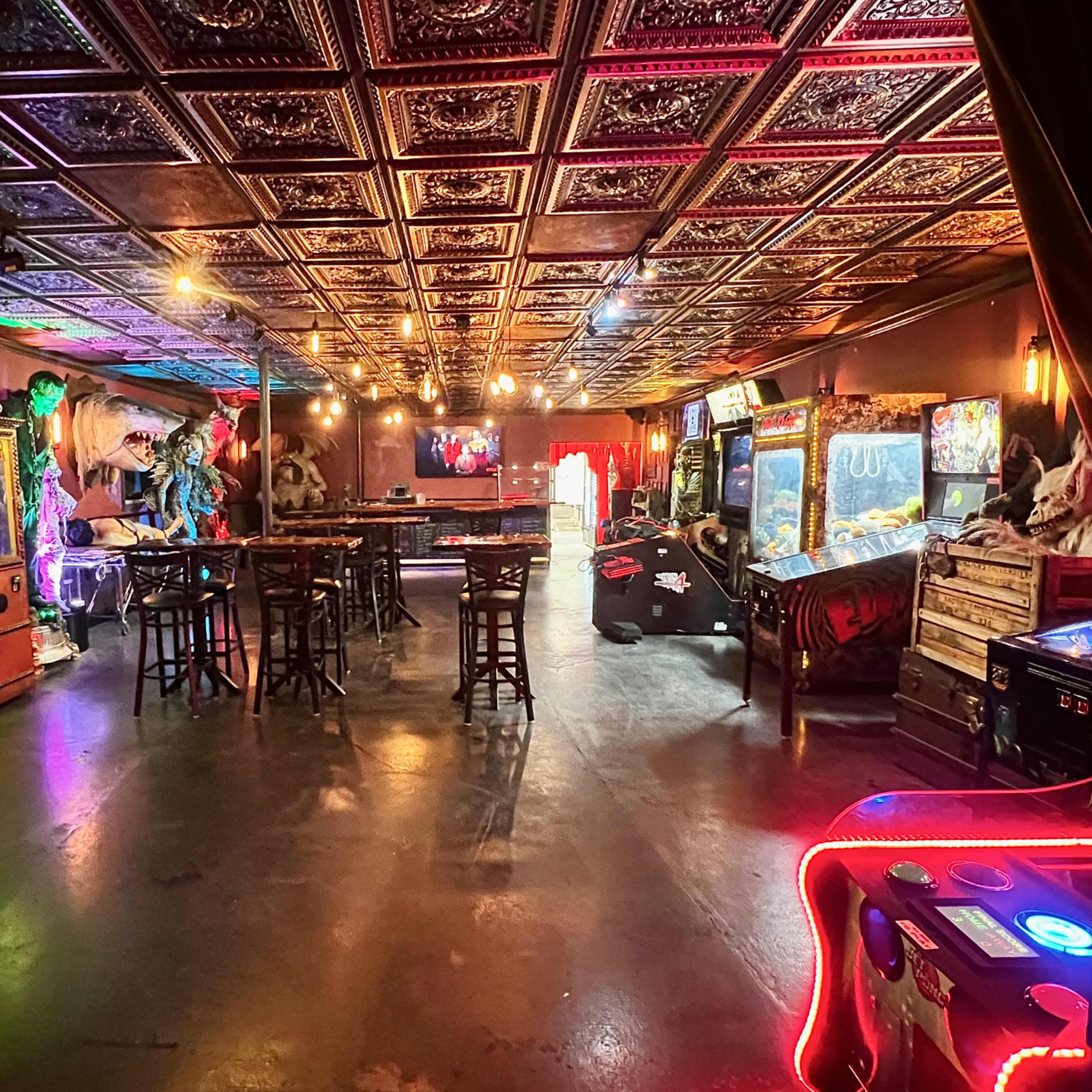 A spacious arcade room with vintage games, a bar area, and decorative lighting on the ceiling.