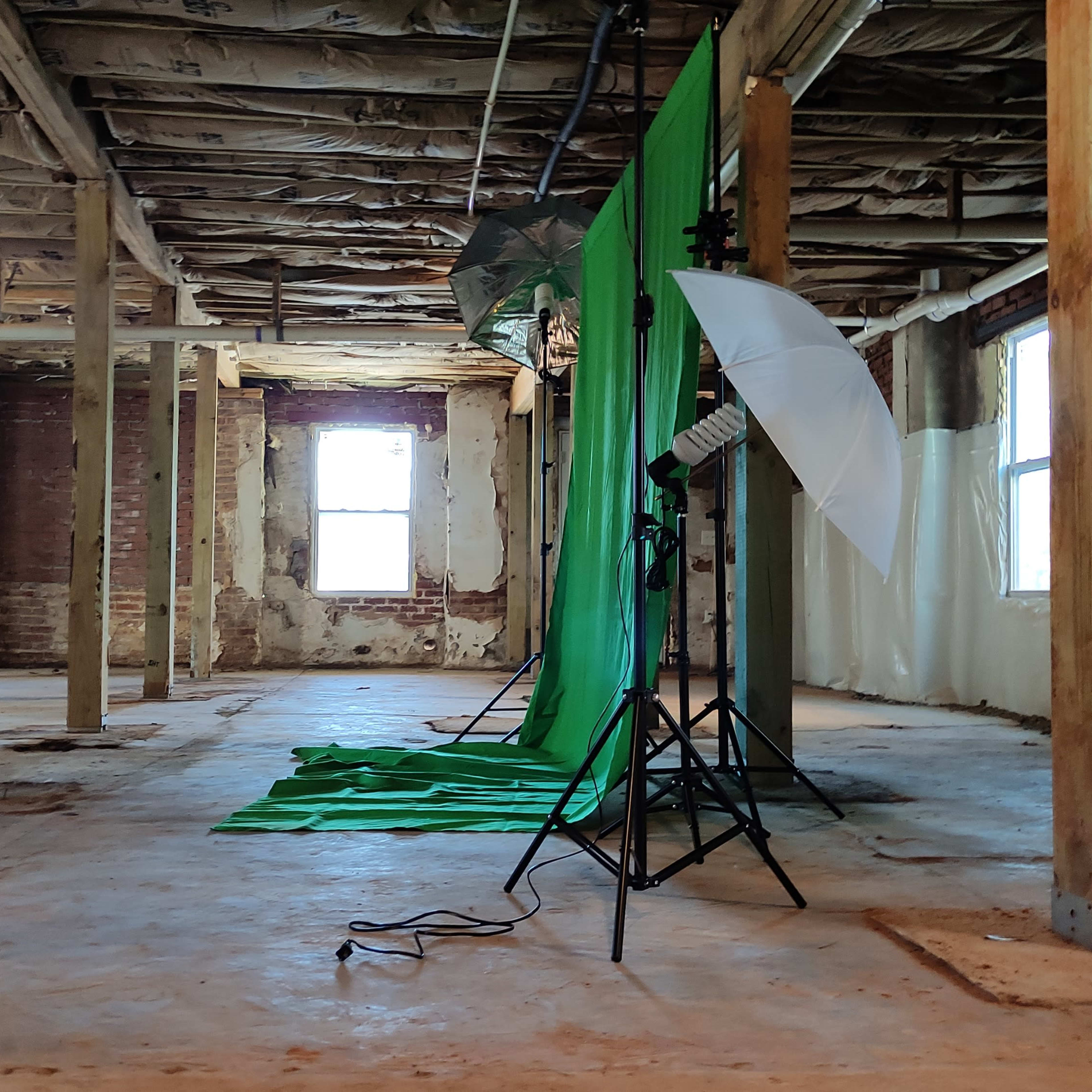 An empty room with wooden beams, bare walls, and green backdrop setup for photography.