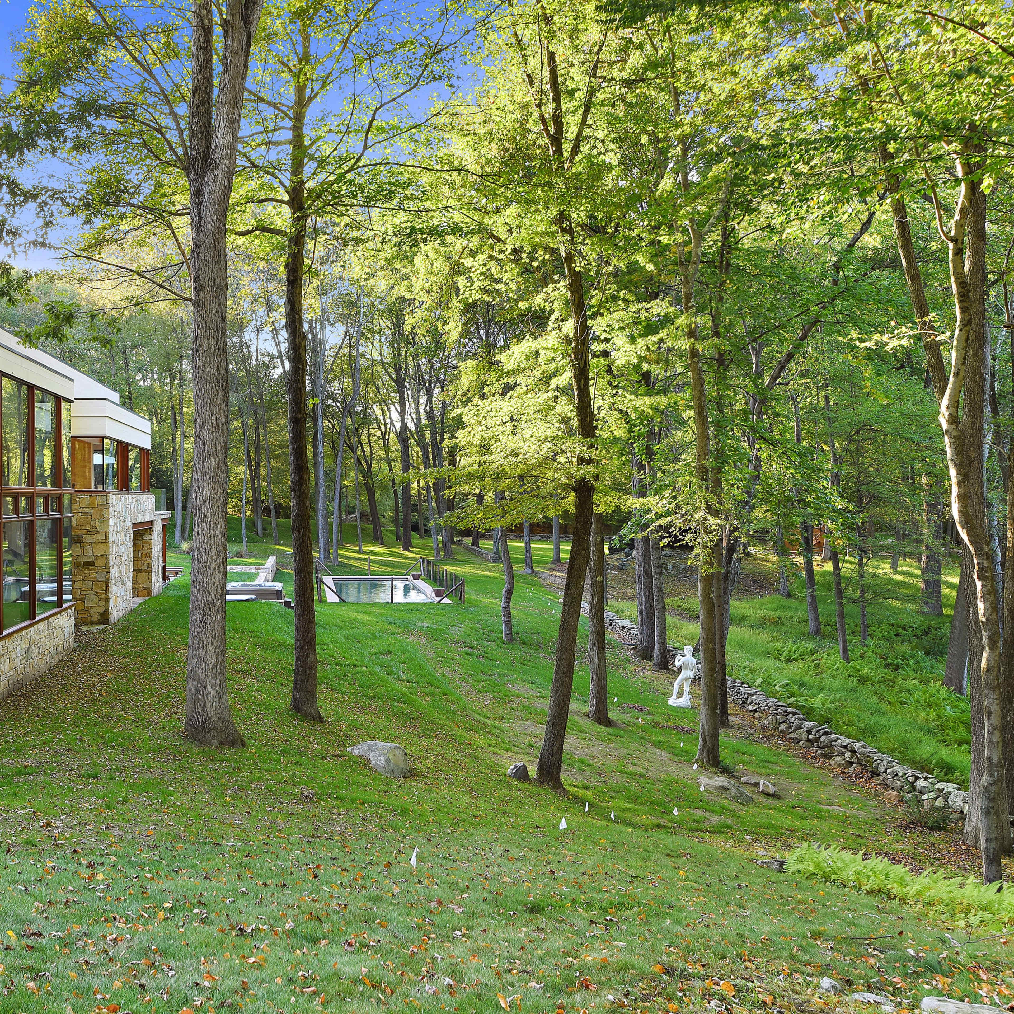 A modern house with large windows set among trees, overlooking a pool and landscaped garden.