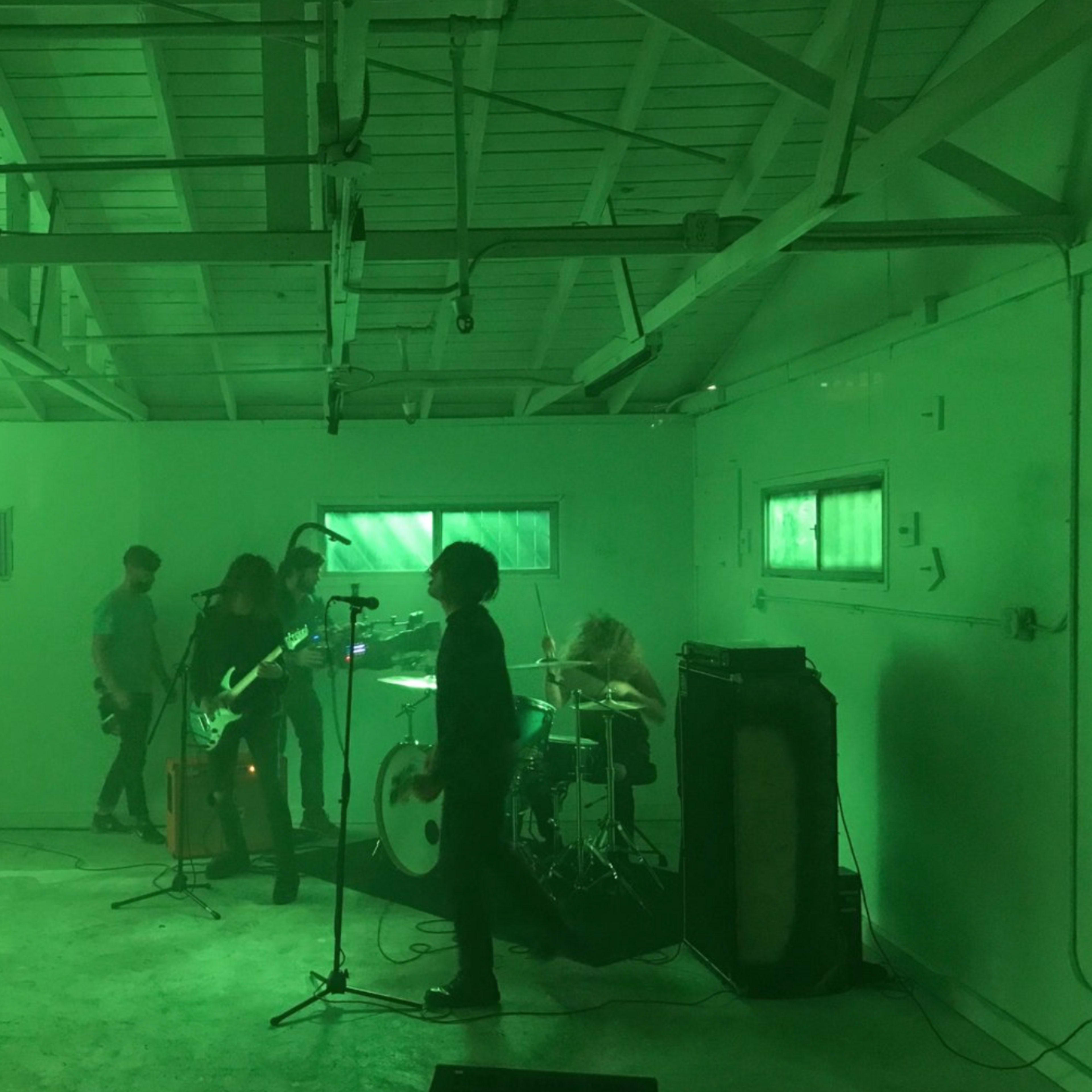 A band performs with green lighting in an industrial-style room.
