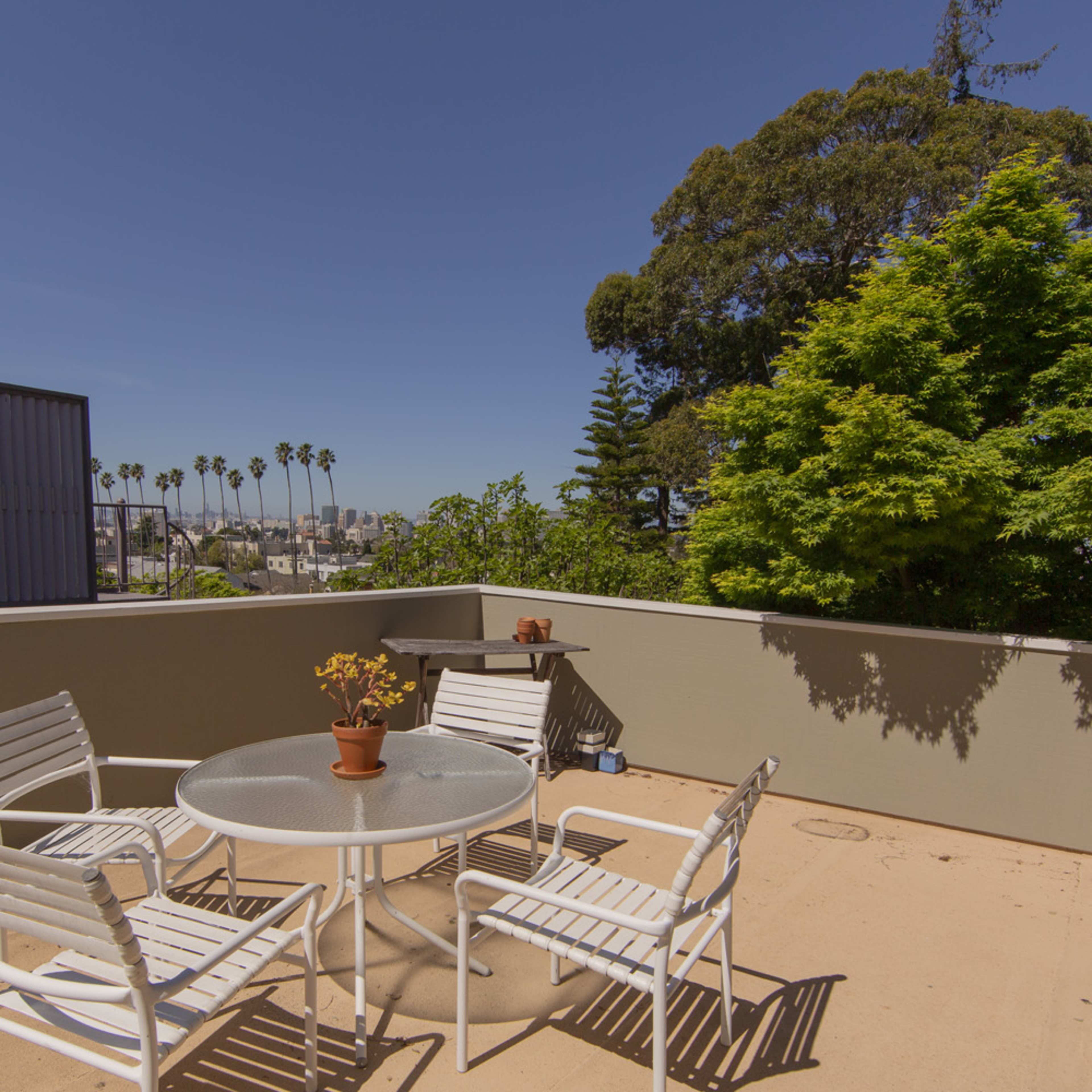 A patio with a round table and four chairs, overlooking a view of palm trees and buildings in the distance.