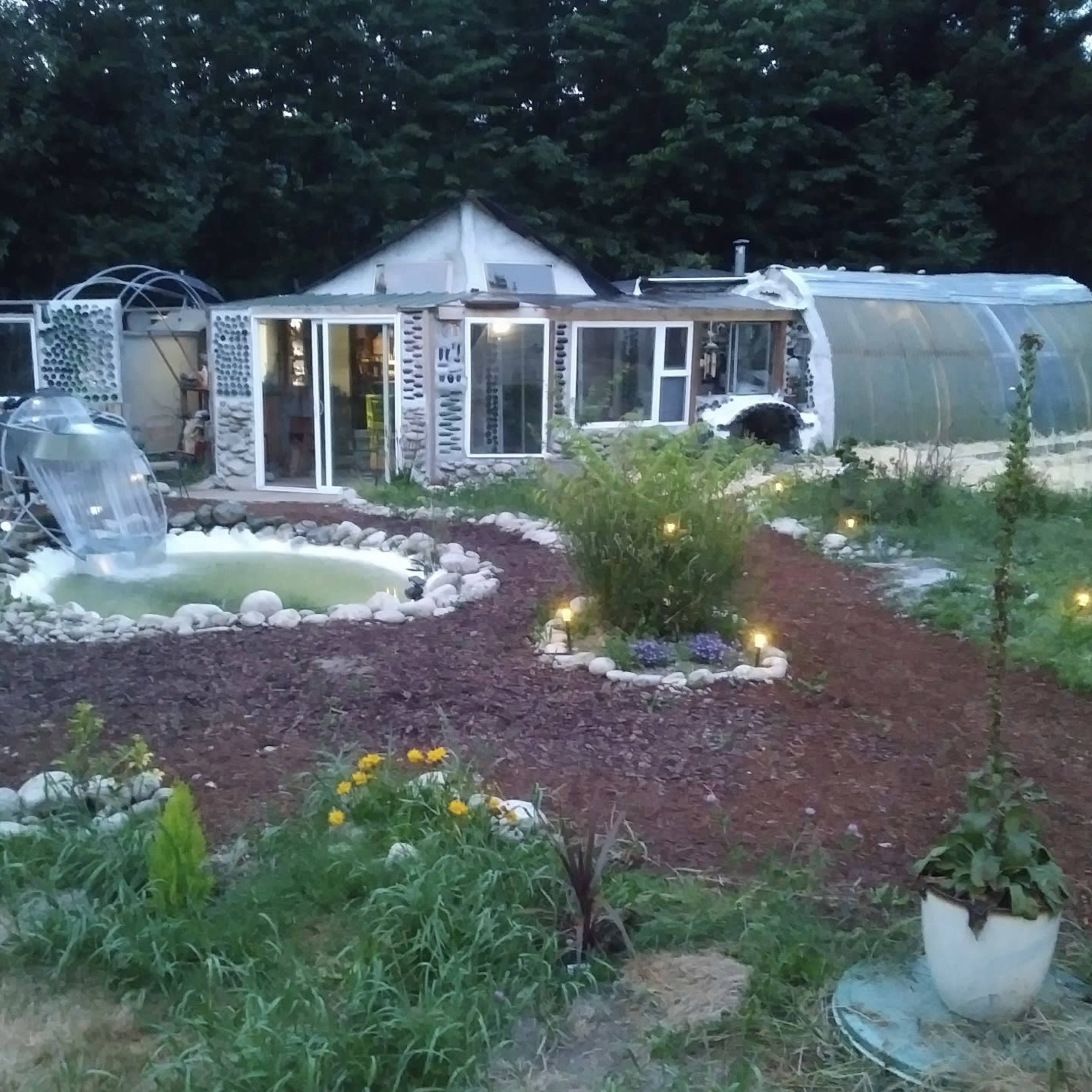 A garden area with a pond, a water slide, and a greenhouse, surrounded by pathways and plants.
