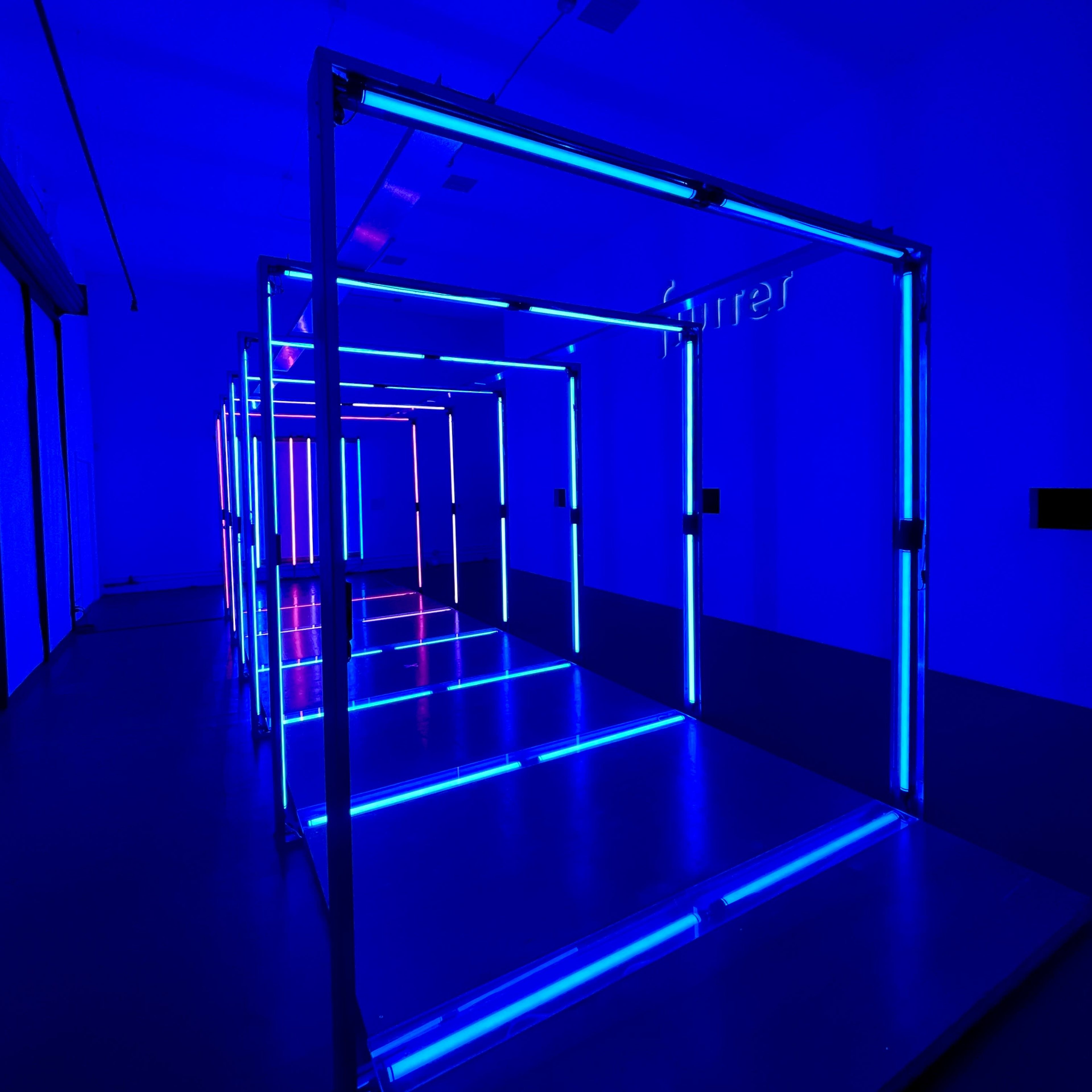 A maze-like structure with metal frames illuminated by blue and white neon lights in a dark room.