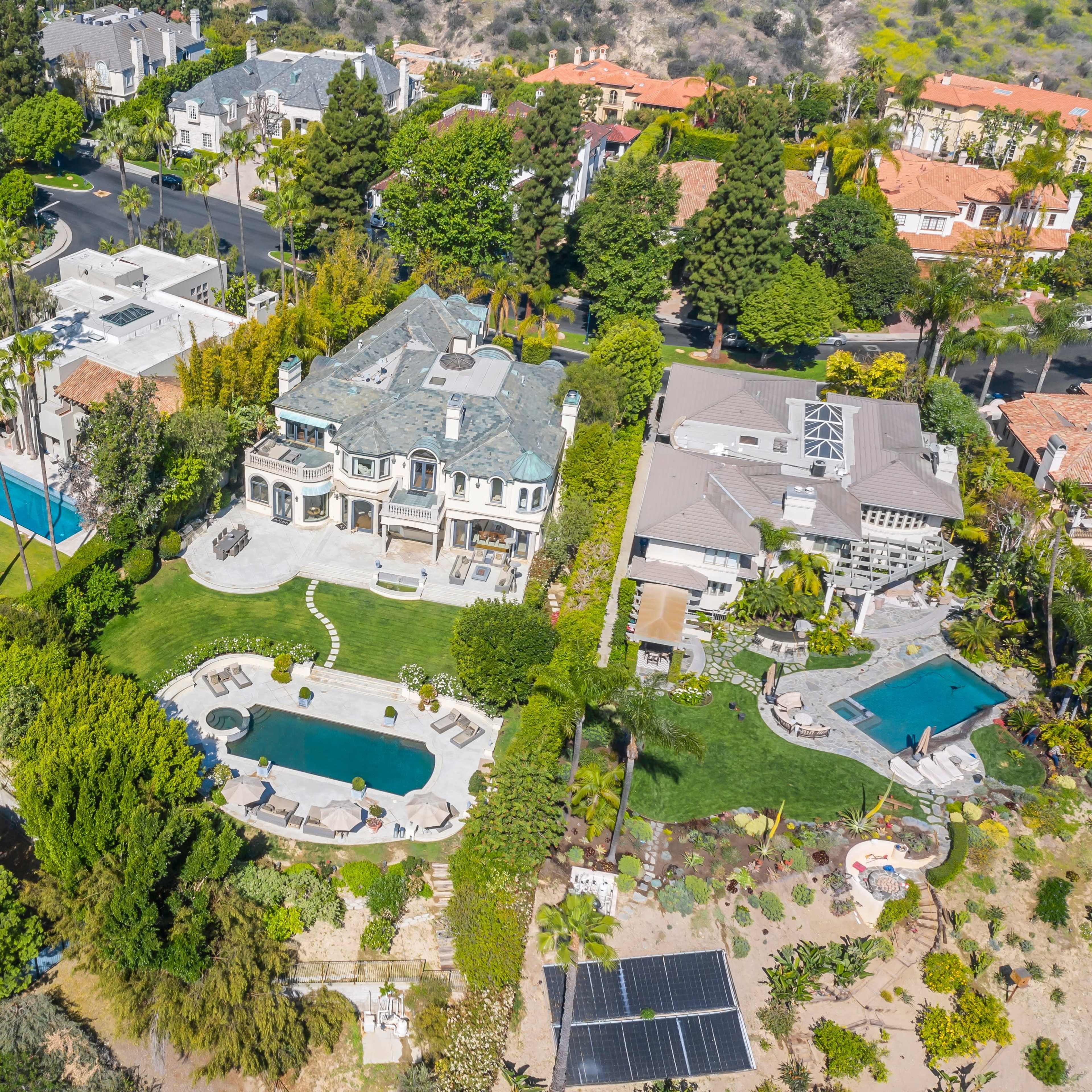 An aerial view of a residential area featuring large homes with pools, landscaped gardens, and palm trees.
