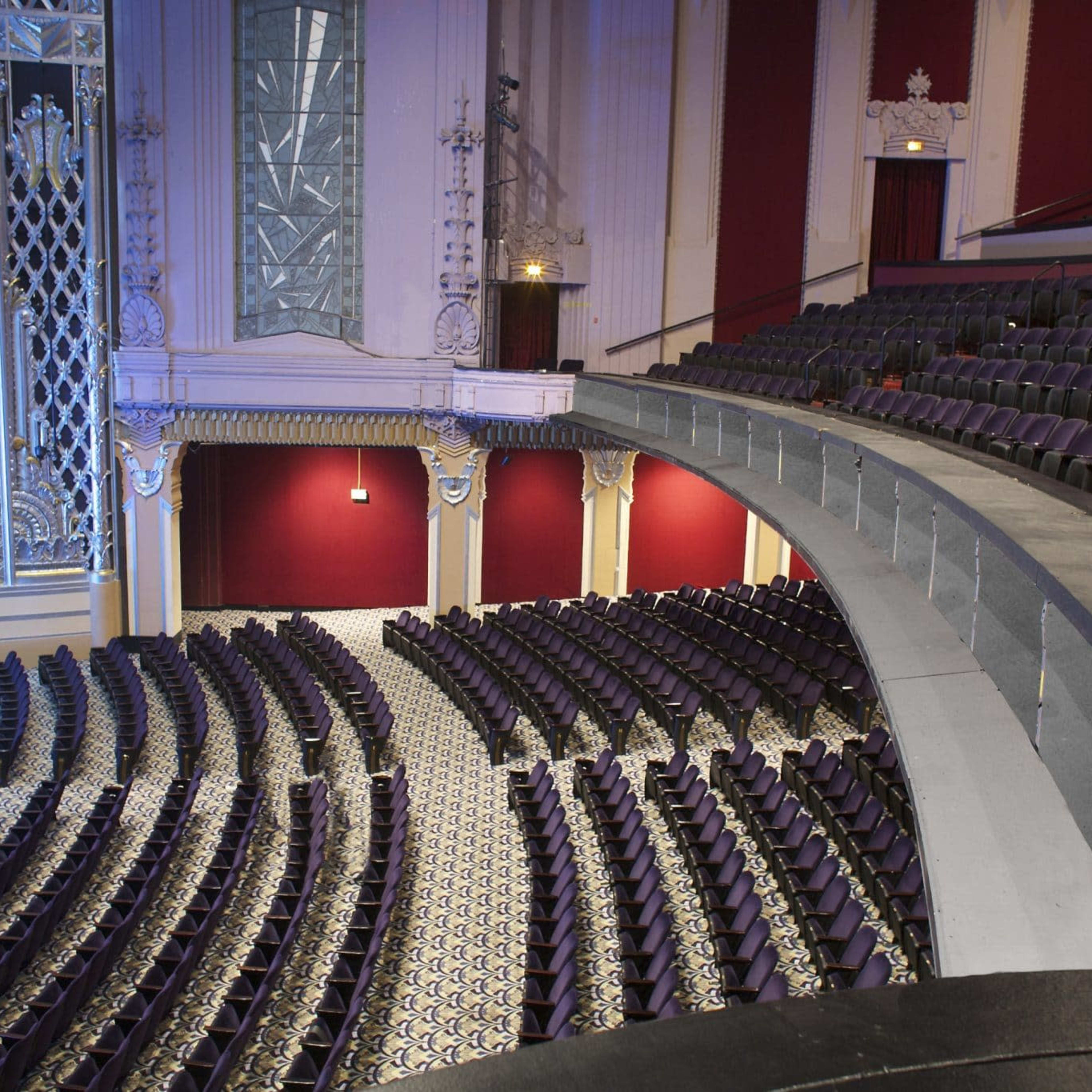 An ornate theater interior with rows of empty purple seats and a decorative stage set up for a performance.