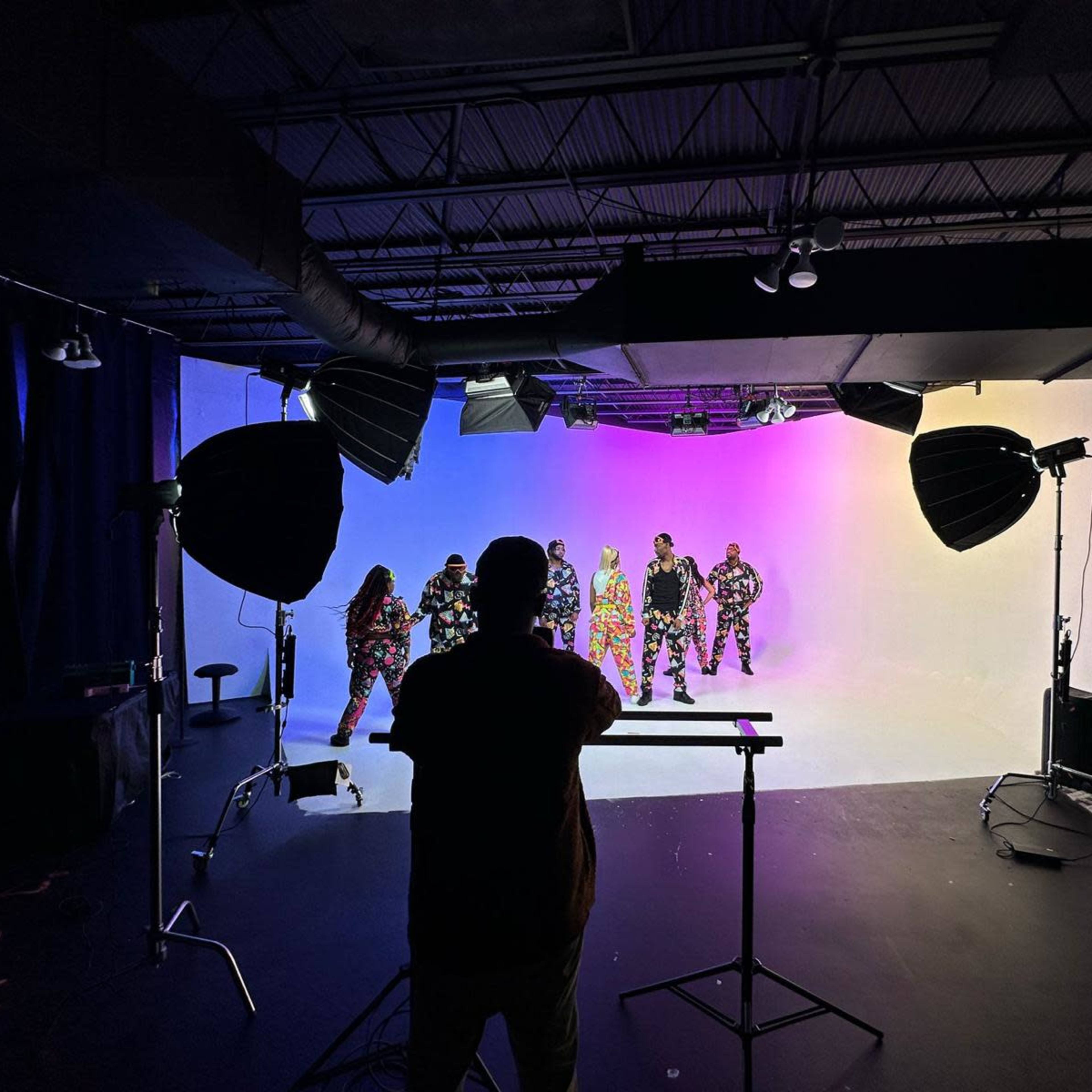 A photographer captures a group of individuals in colorful outfits against a lit backdrop in a studio.