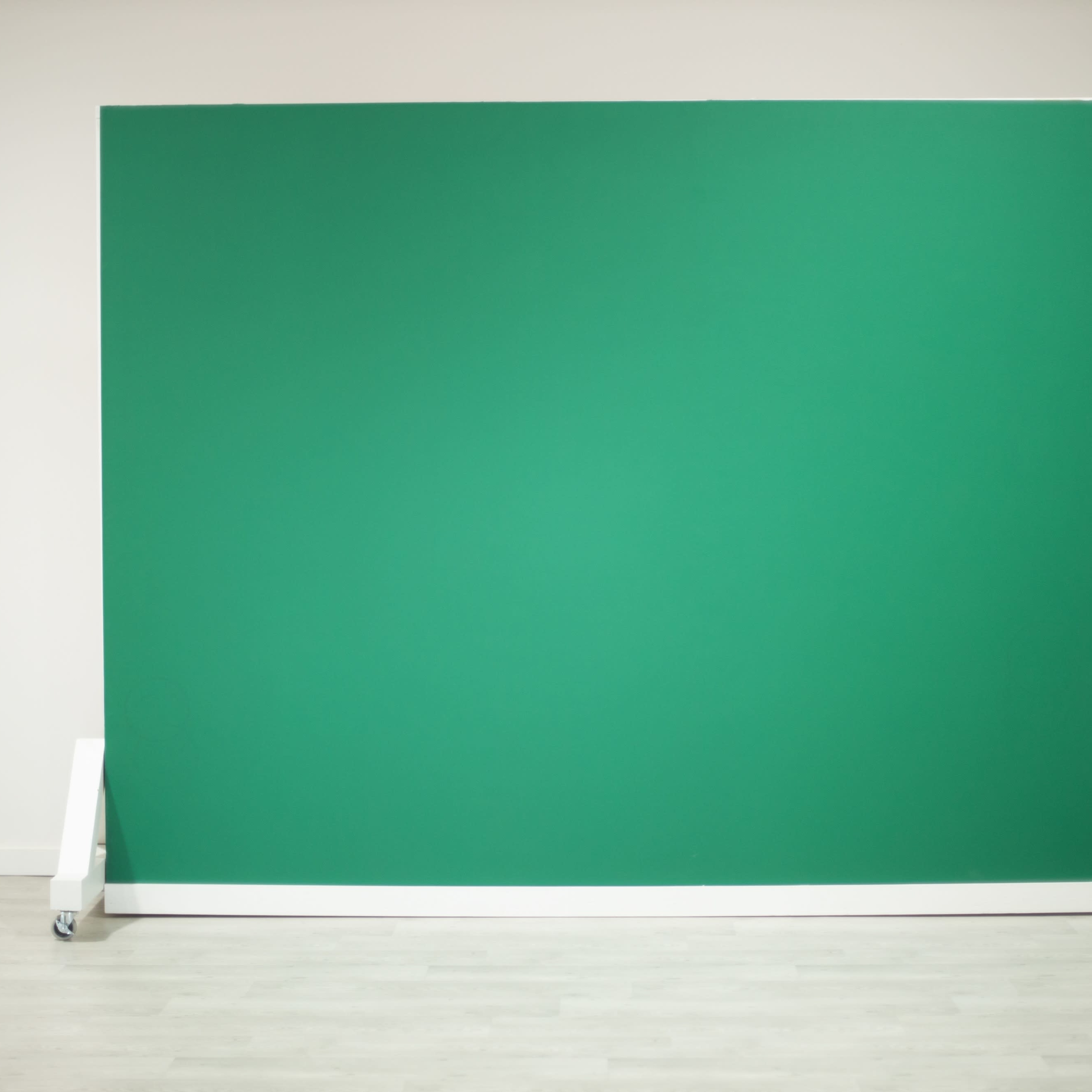A green backdrop setup on wheels against a plain wall.