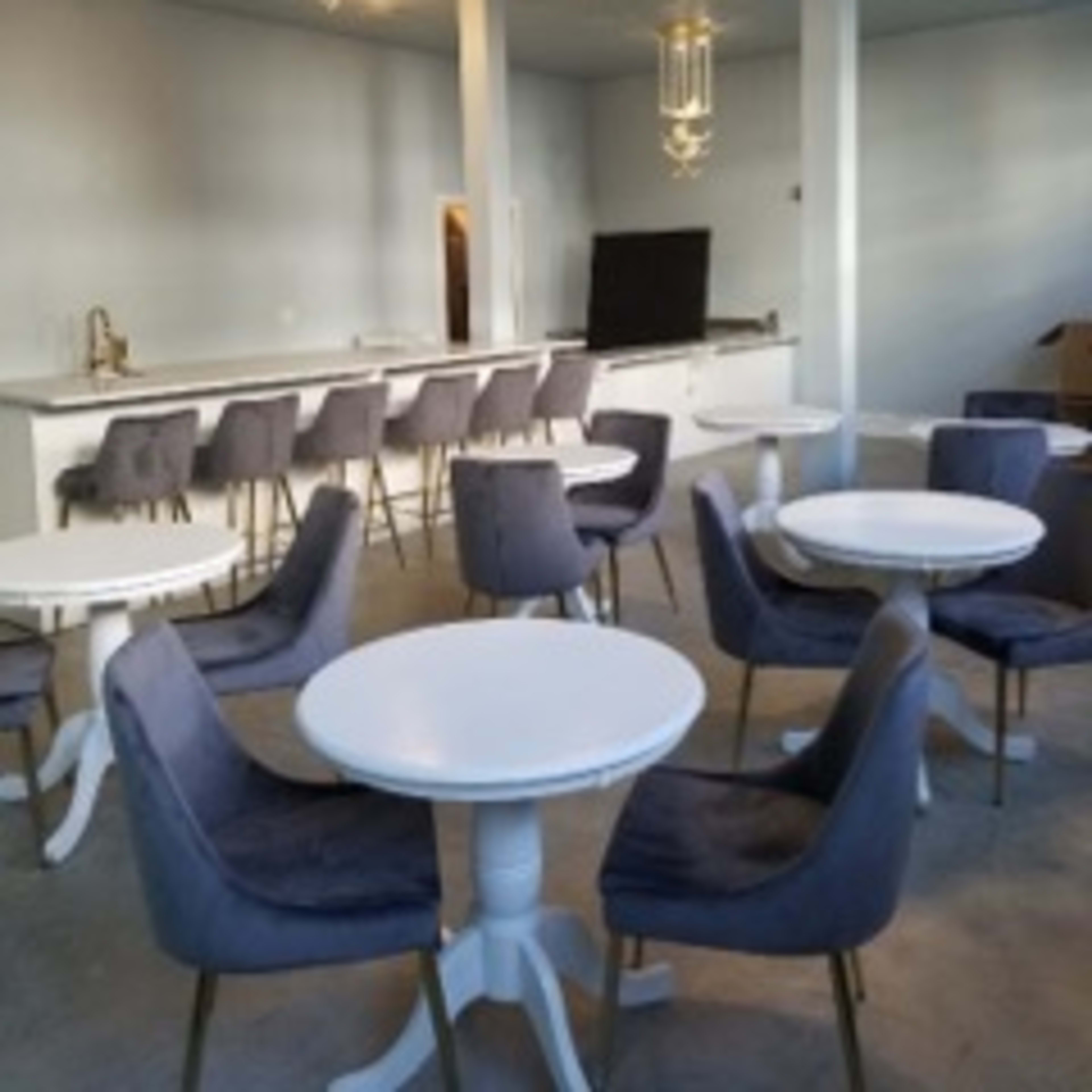 A modern interior featuring several small round tables with chairs arranged around a counter area in a brightly lit space.