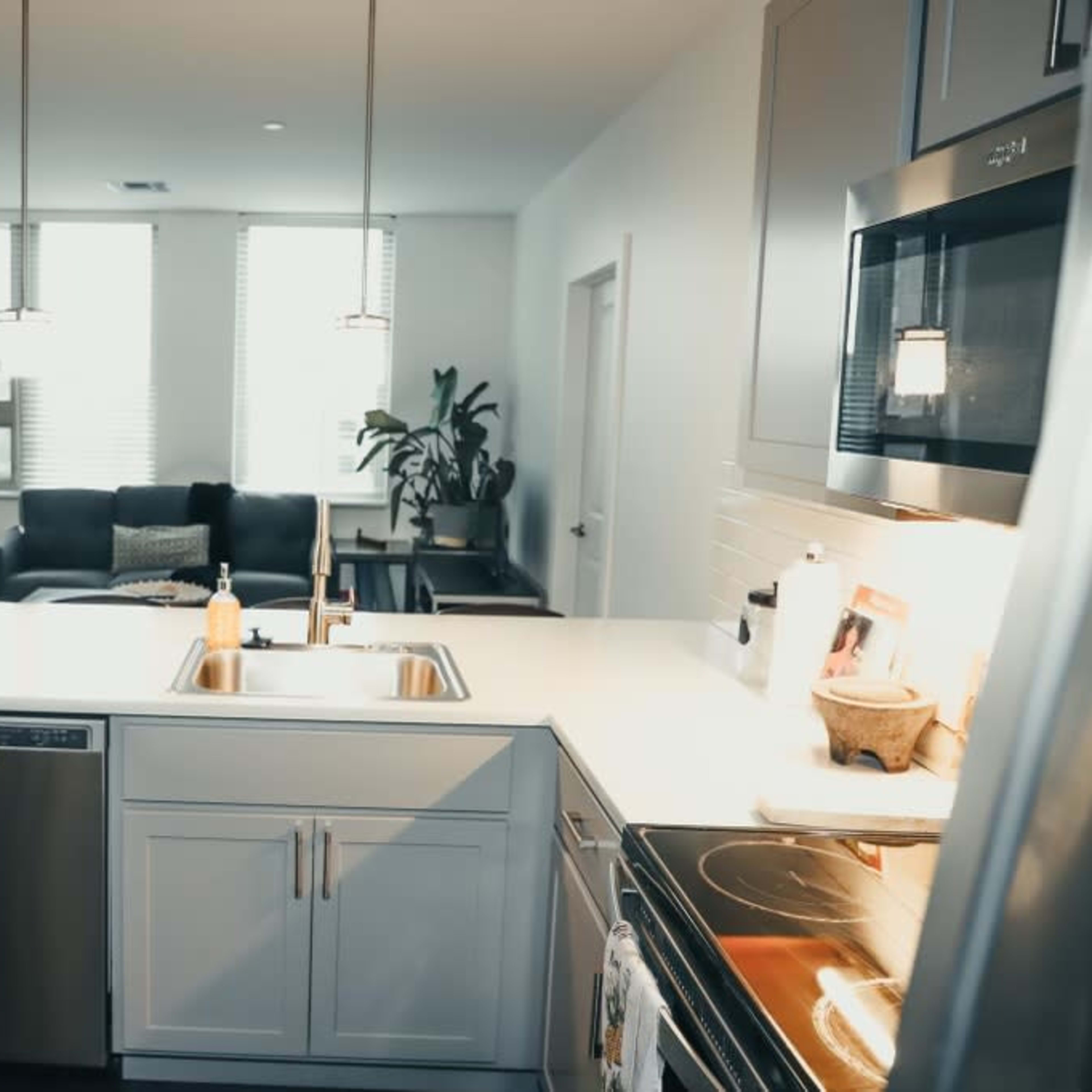 A modern kitchen with a central island, stainless steel appliances, and a living area visible in the background.