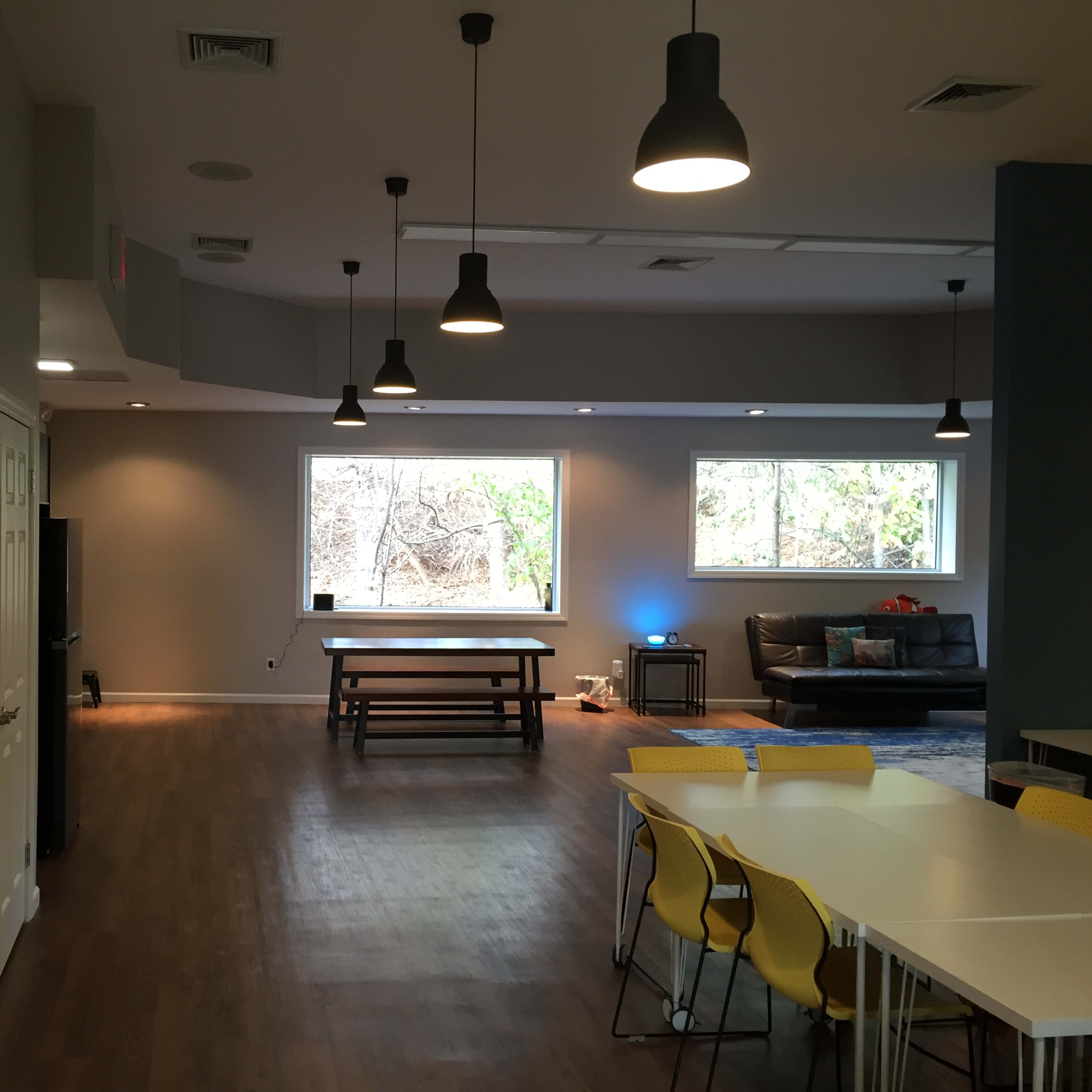 A spacious, modern room with a dining table, seating area, and bright windows overlooking a wooded area.