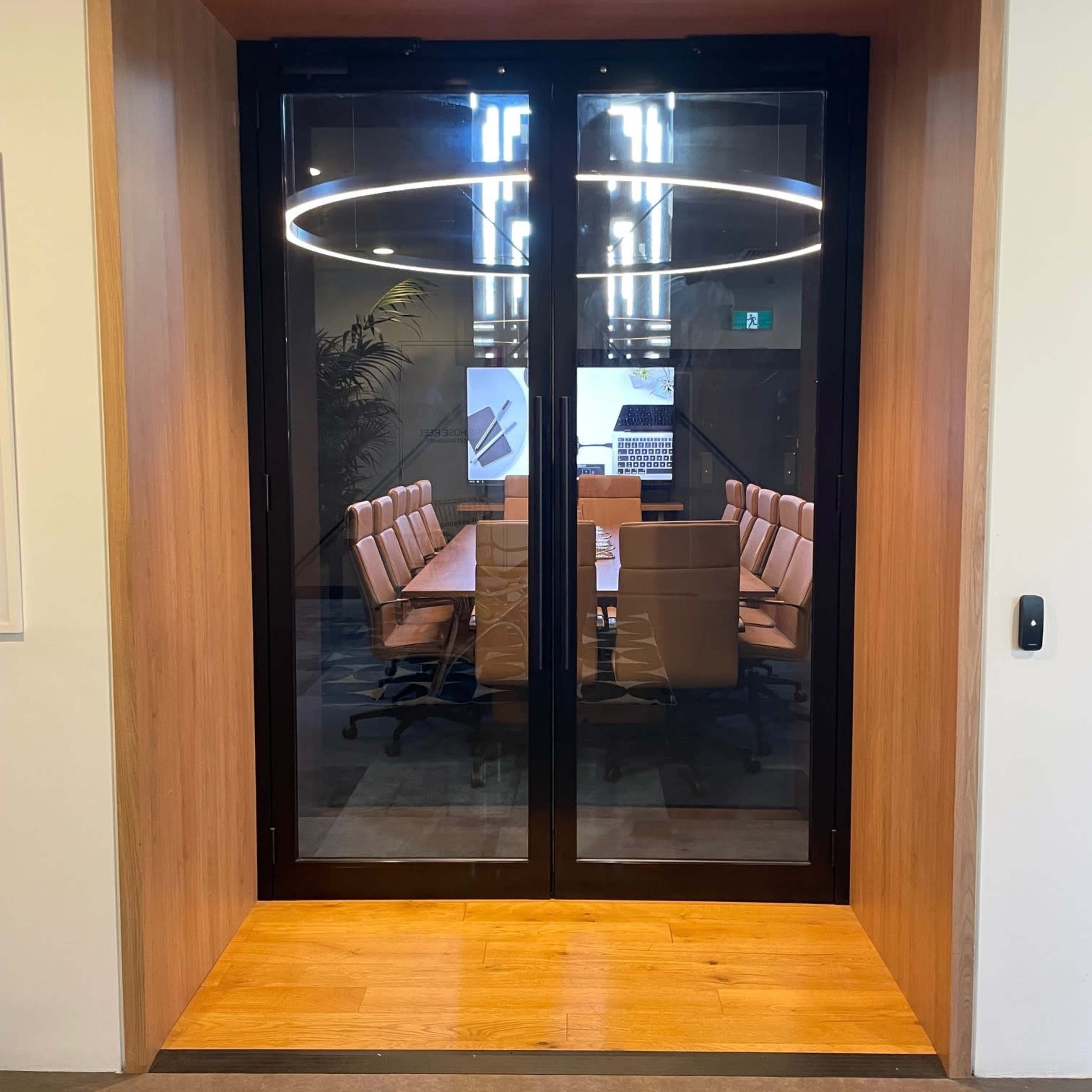 A glass door opening to a modern conference room with a long table and several chairs.