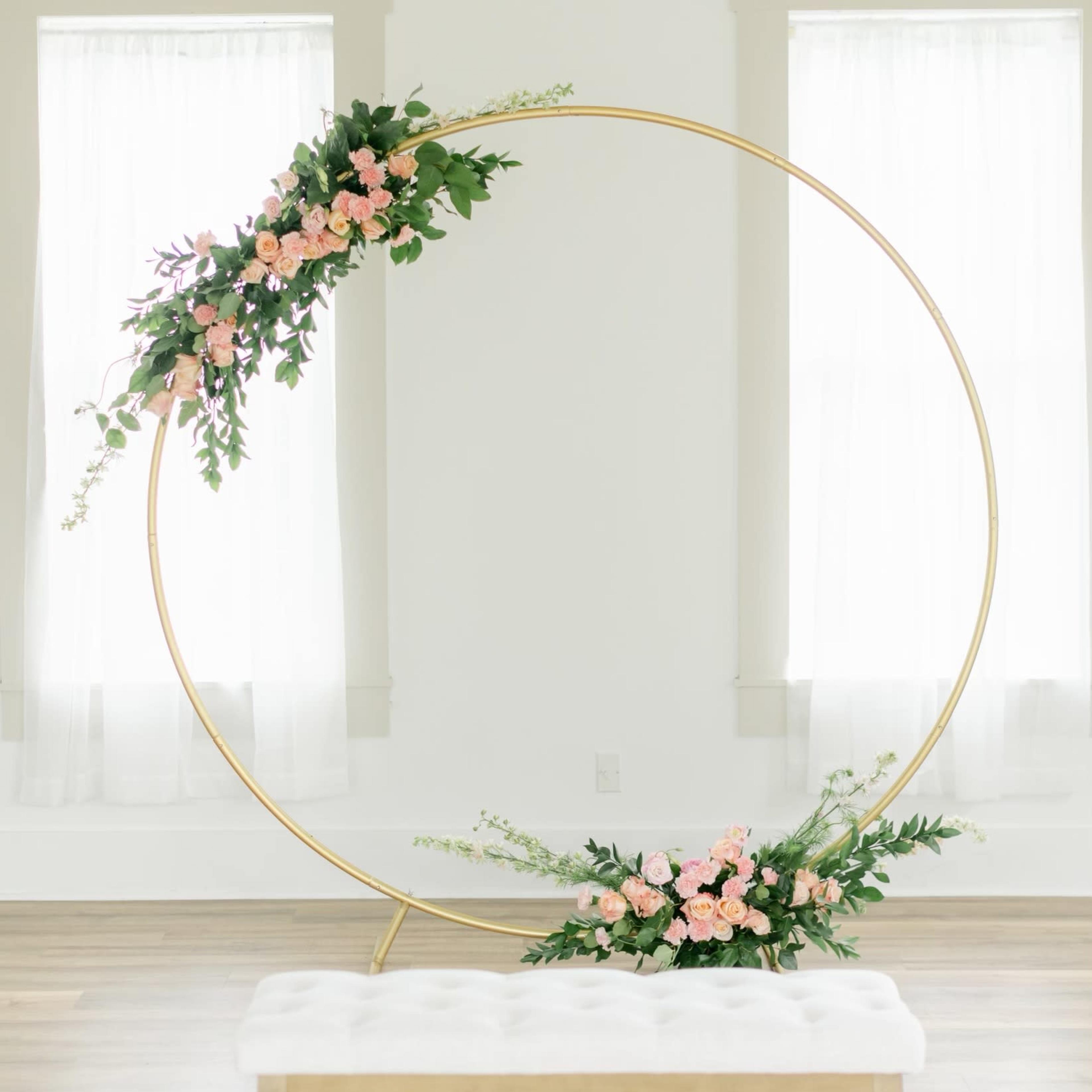 A circular gold frame adorned with pink flowers is positioned beside a white bench in a room with large windows.