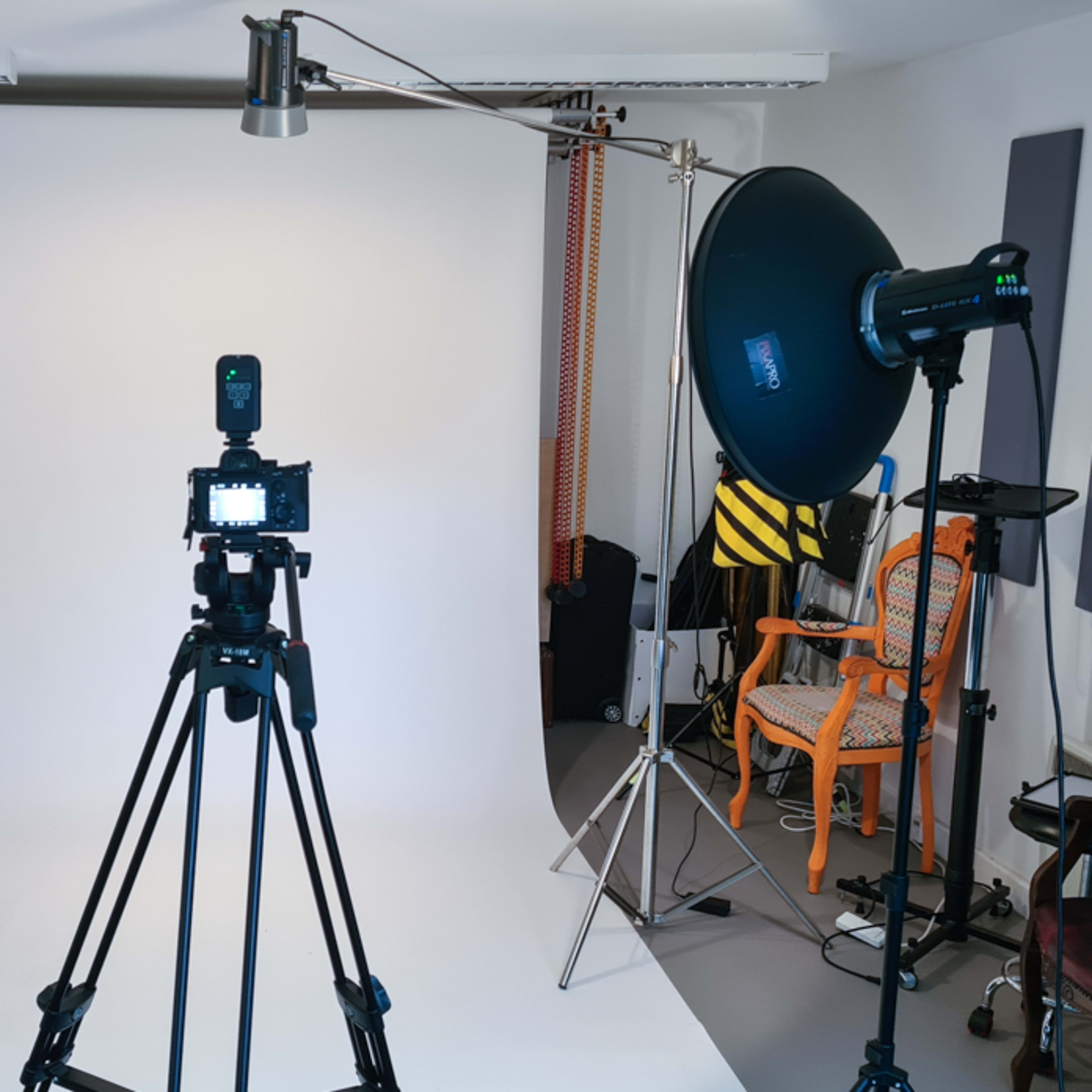 A photography studio setup with a camera on a tripod facing a plain backdrop illuminated by softbox lights.