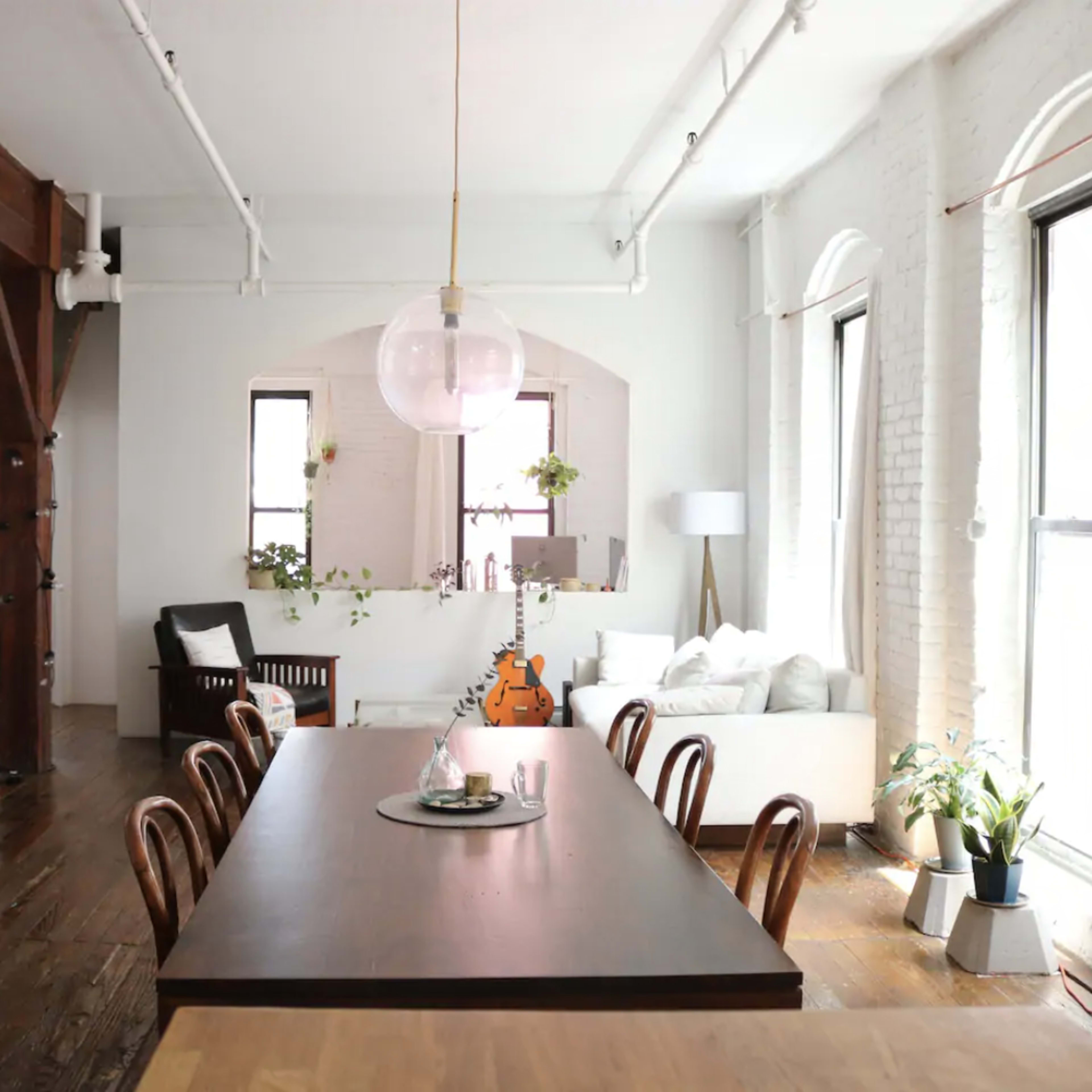 A spacious, well-lit room with a long dining table, wooden beams, and a mix of modern and rustic furnishings.