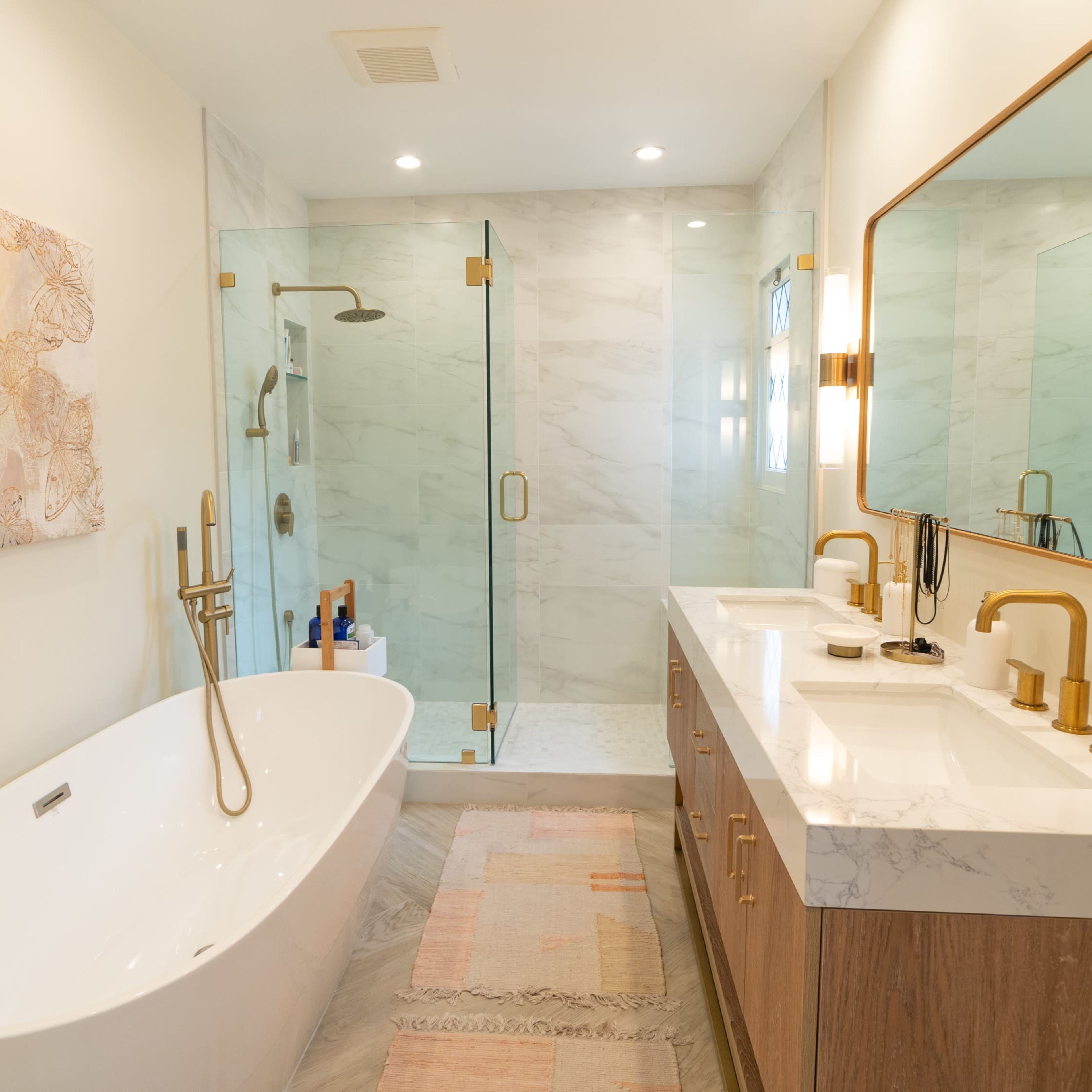A modern bathroom with a freestanding bathtub, double vanity sinks, and a glass shower enclosure, featuring marble accents and wooden cabinetry.