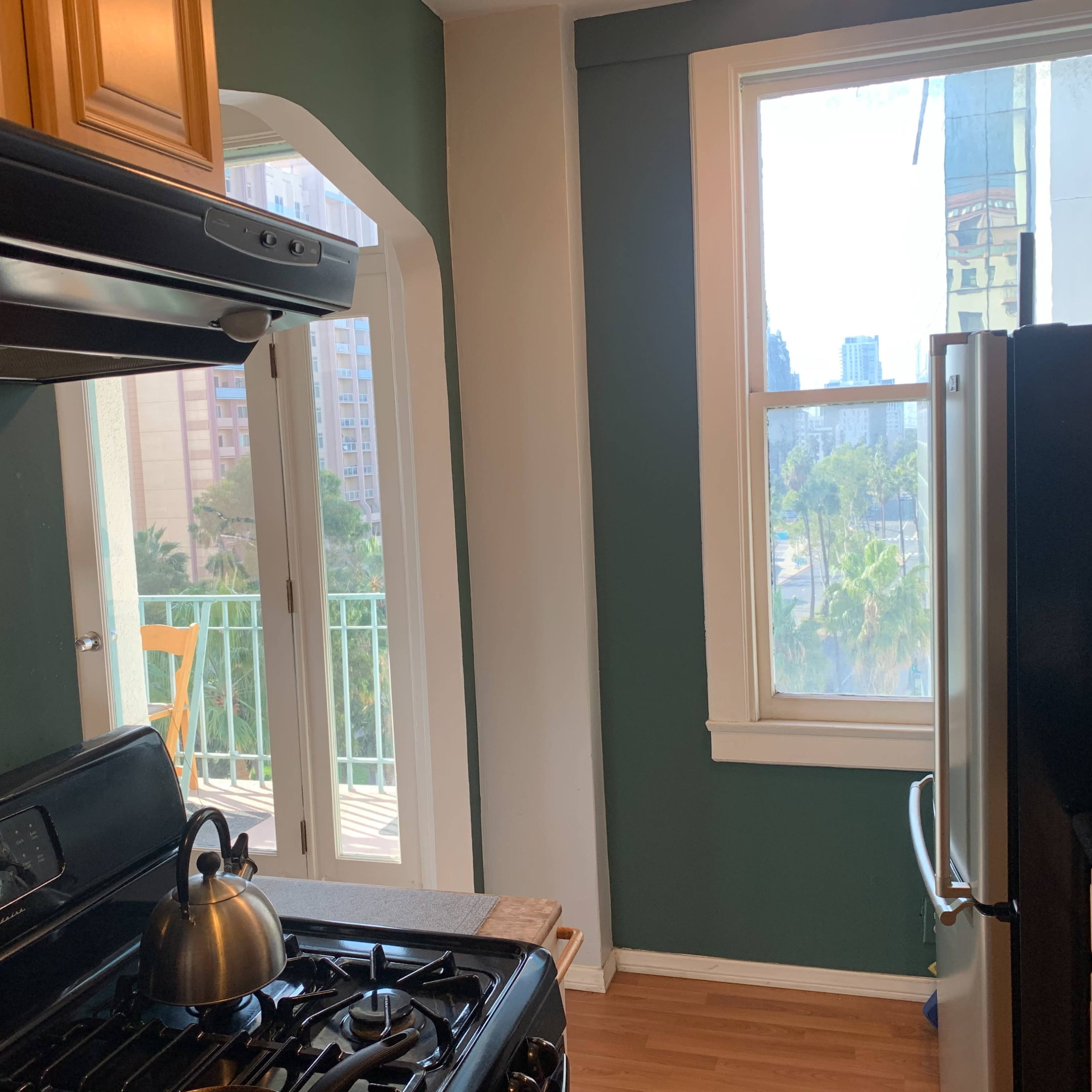 A kitchen featuring a gas stove, a stainless-steel refrigerator, and a large window with a view of buildings and greenery outside.