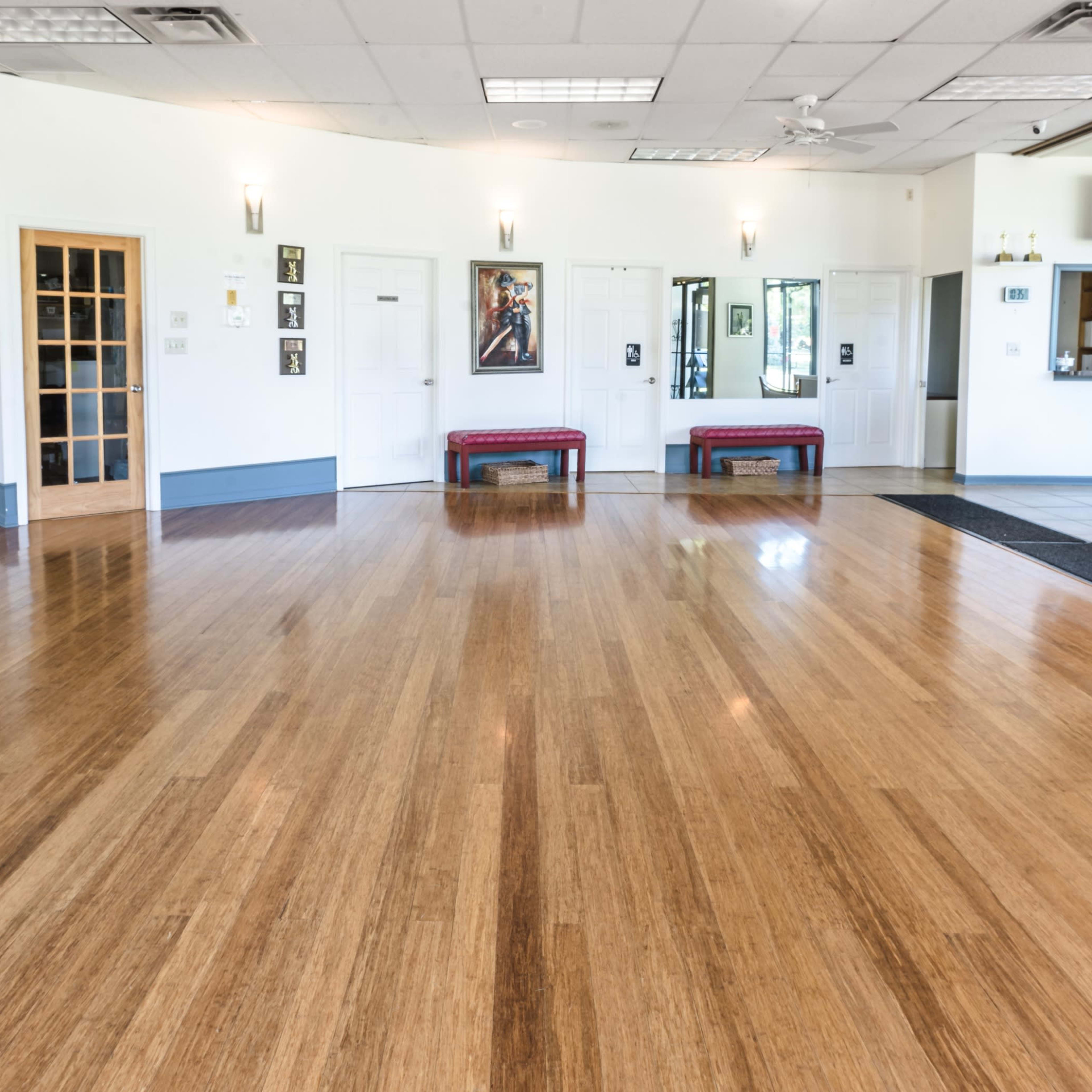 A spacious interior room with polished bamboo flooring, mirrored walls, and a seating area with benches and a dining space in the background.