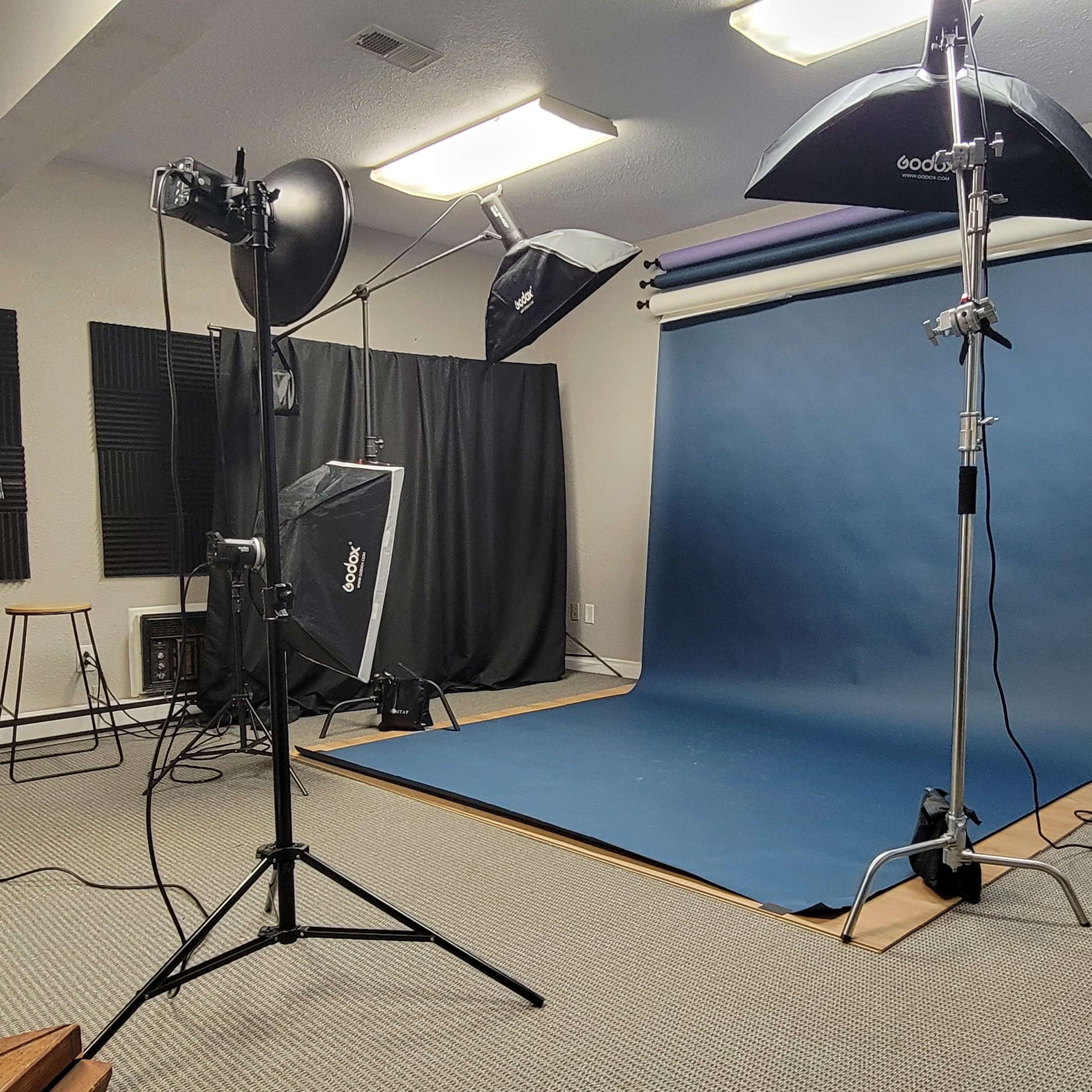 A photography studio with a blue backdrop, various lighting equipment, and a chair in the corner.