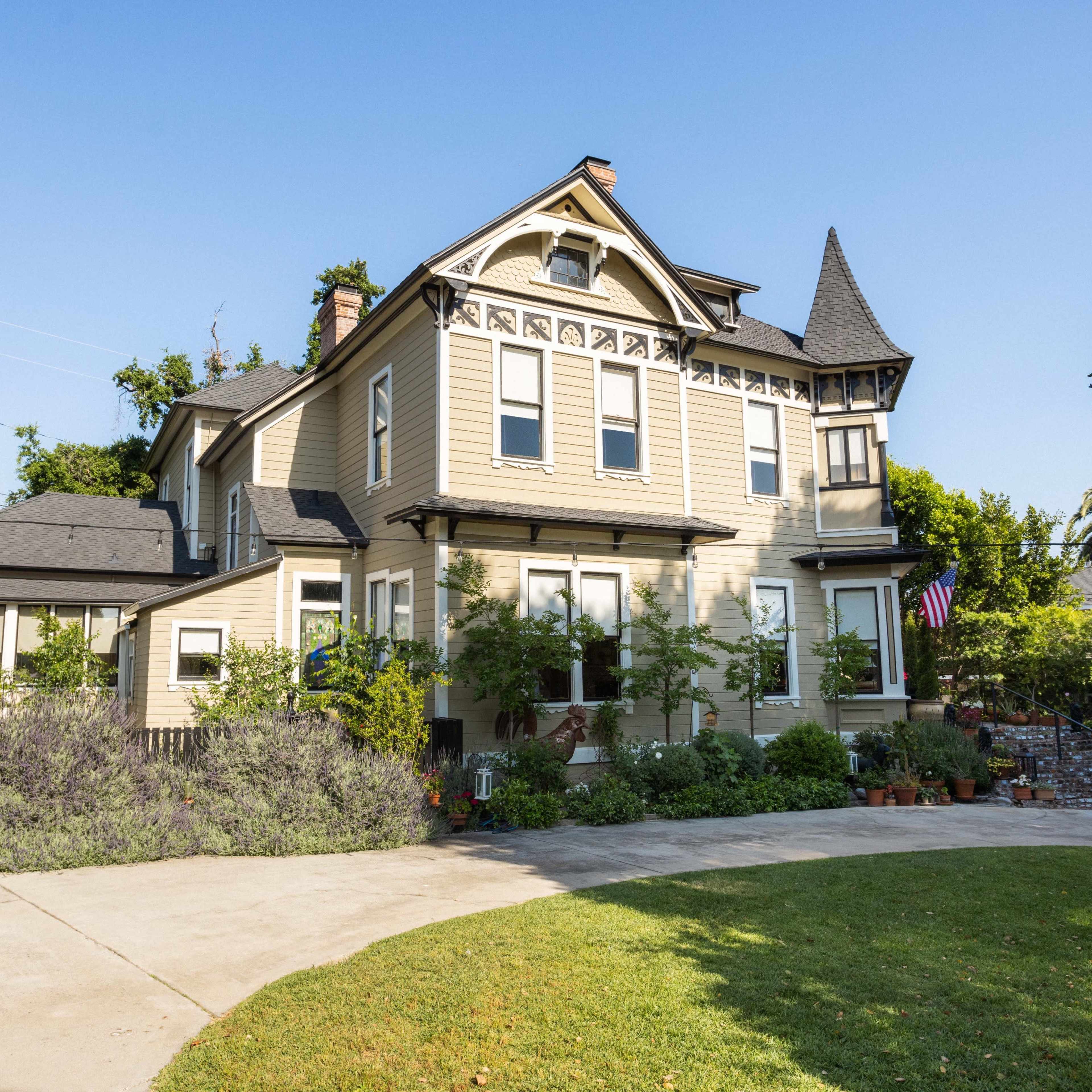 A large Victorian-style house with a pointed rooftop and a circular driveway surrounded by landscaped greenery.