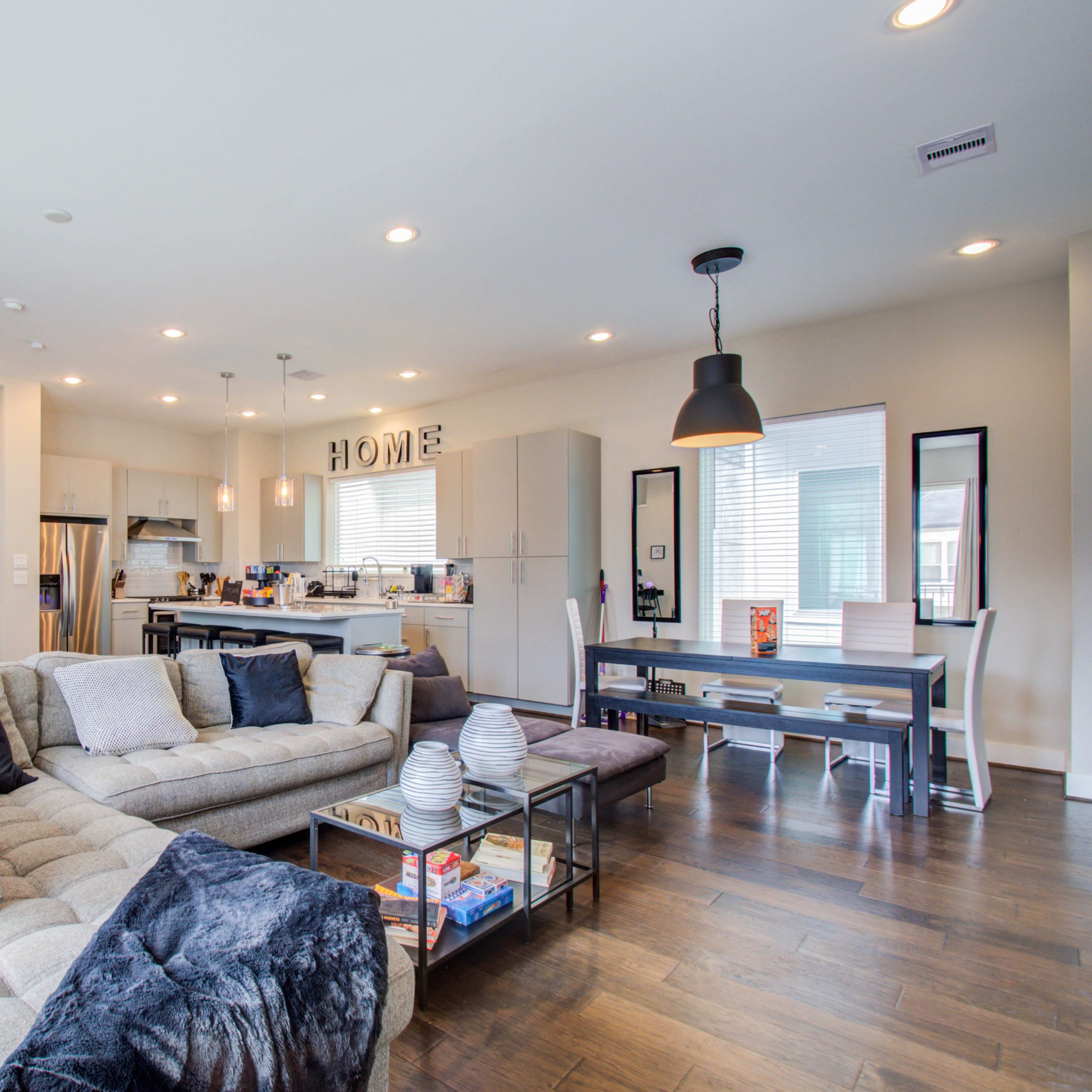 A modern open-concept living space featuring a comfortable sofa, a dining table, and a kitchen area with white cabinets.