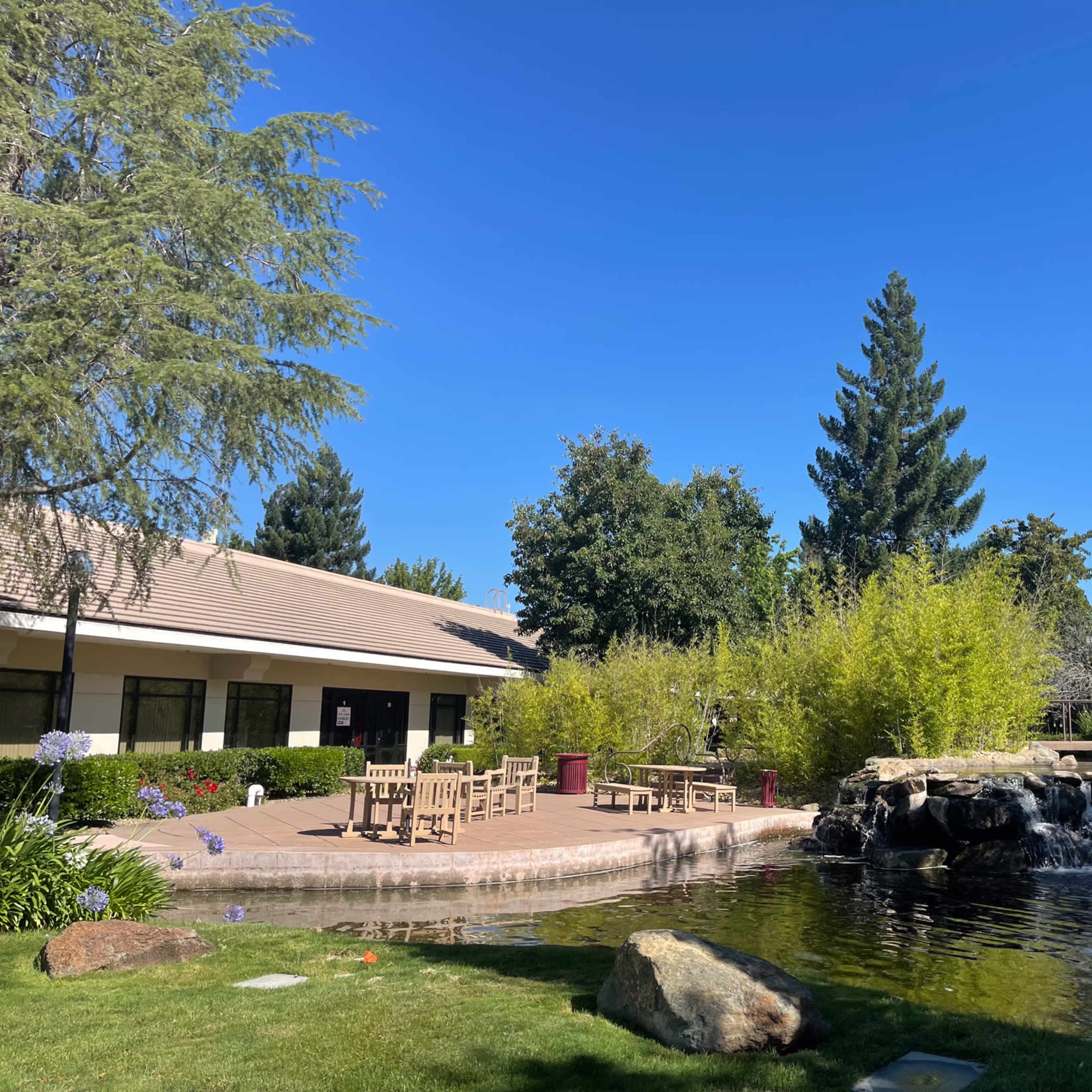 A landscaped courtyard features a pond with a waterfall, surrounded by seating areas and greenery under a clear blue sky.