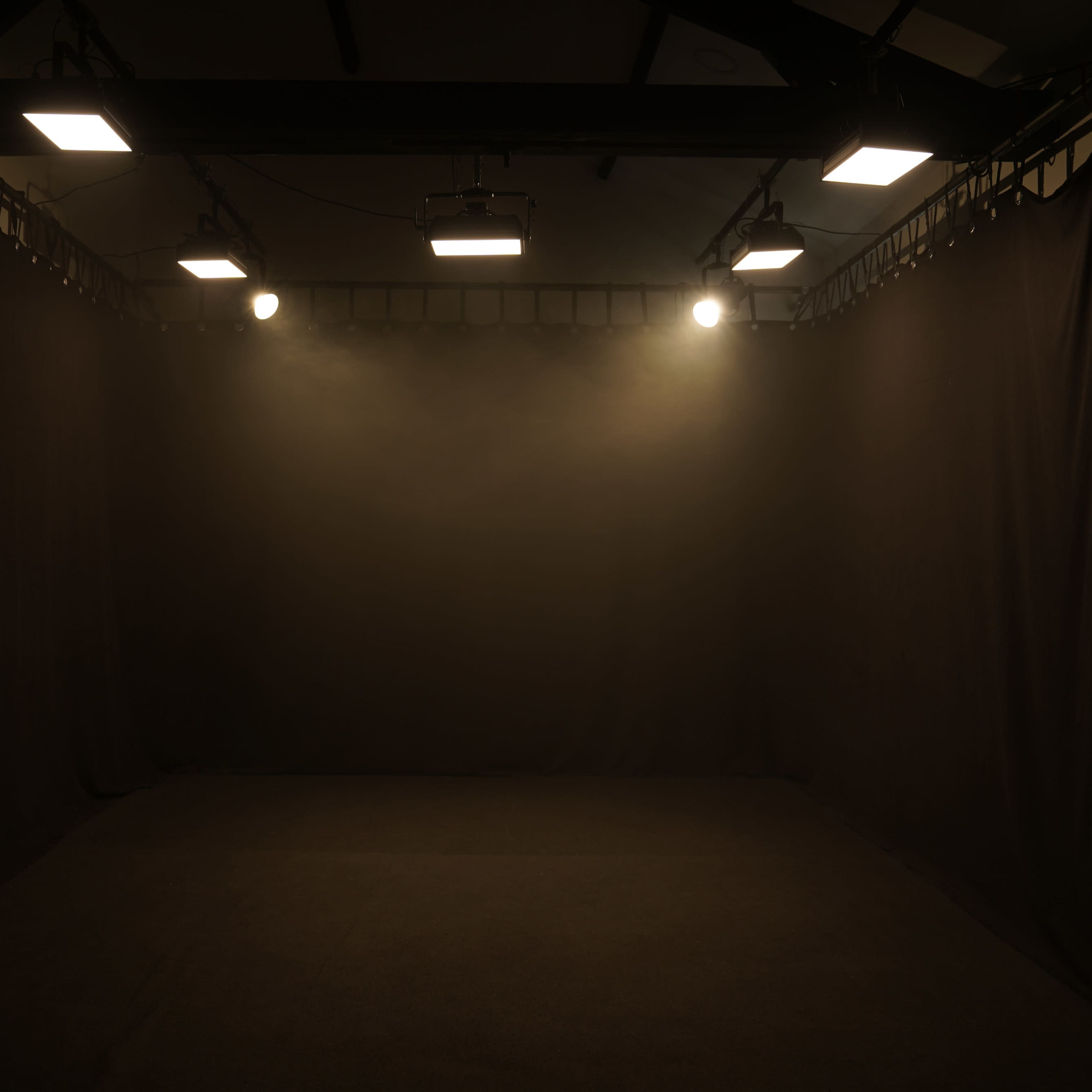 An empty room with dark walls and ceiling, illuminated by overhead lights creating a focused glow in the center.