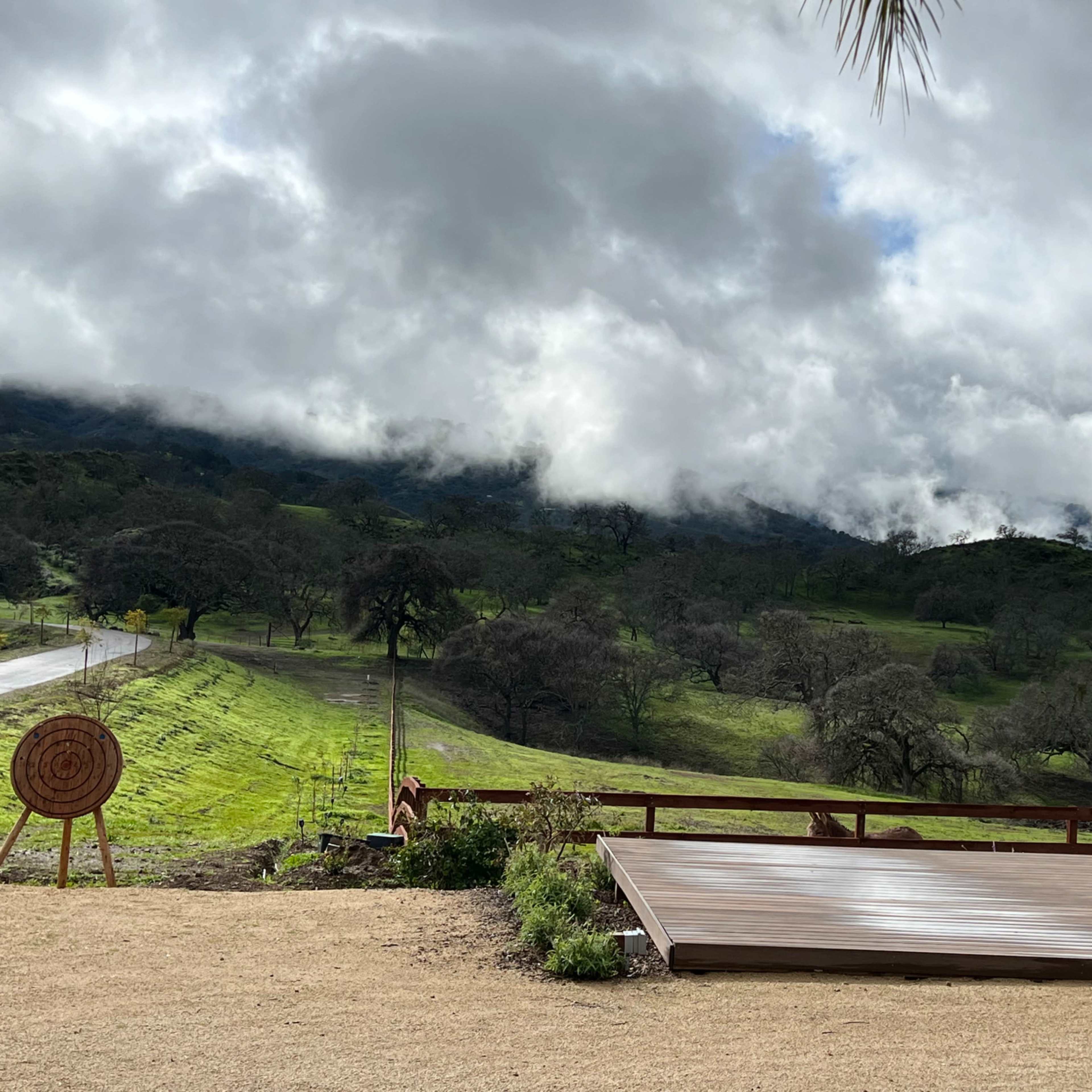 A wooden platform is situated in a grassy area overlooking a hilly landscape under a cloudy sky.