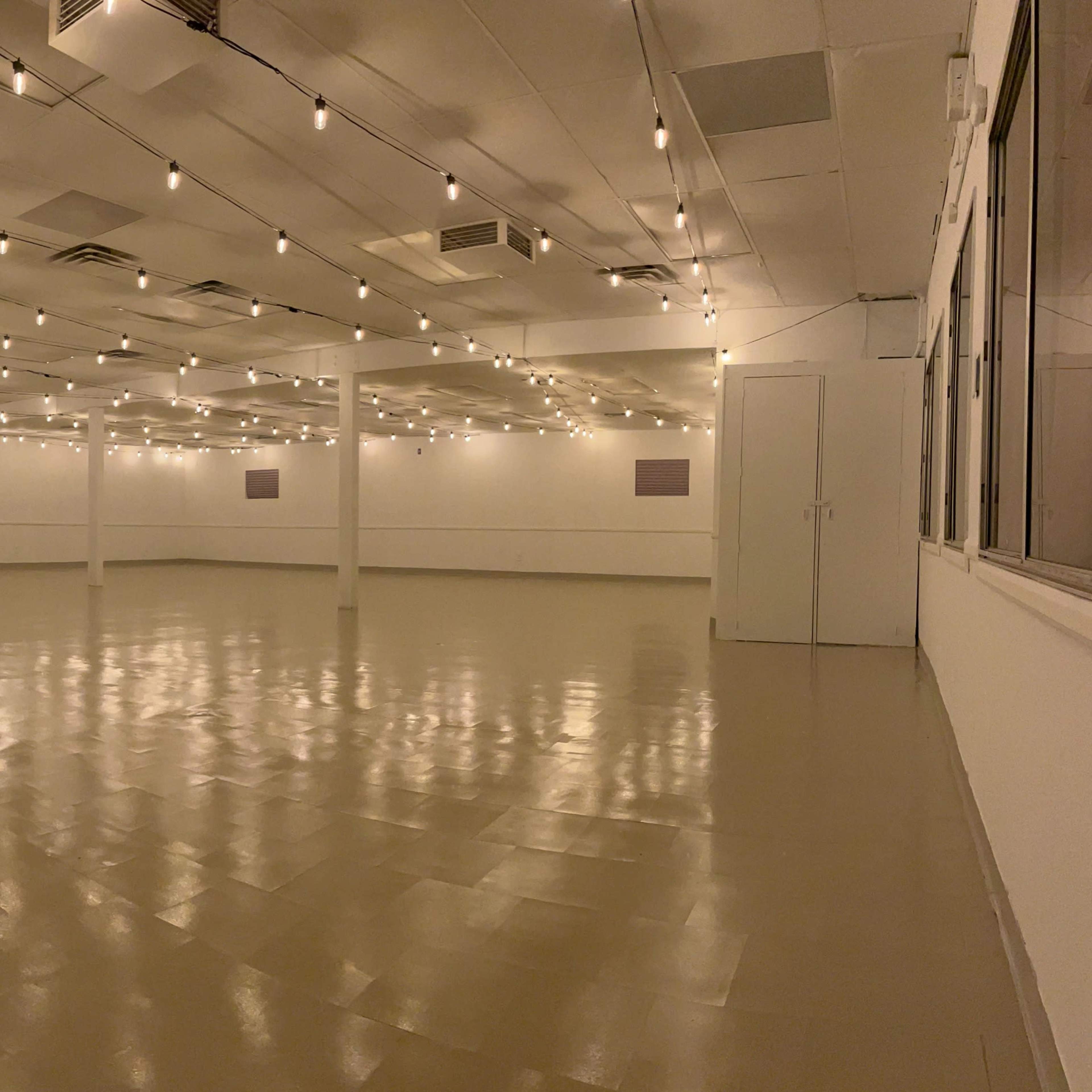A spacious, empty room with polished floors and dim, string lights hanging from the ceiling.