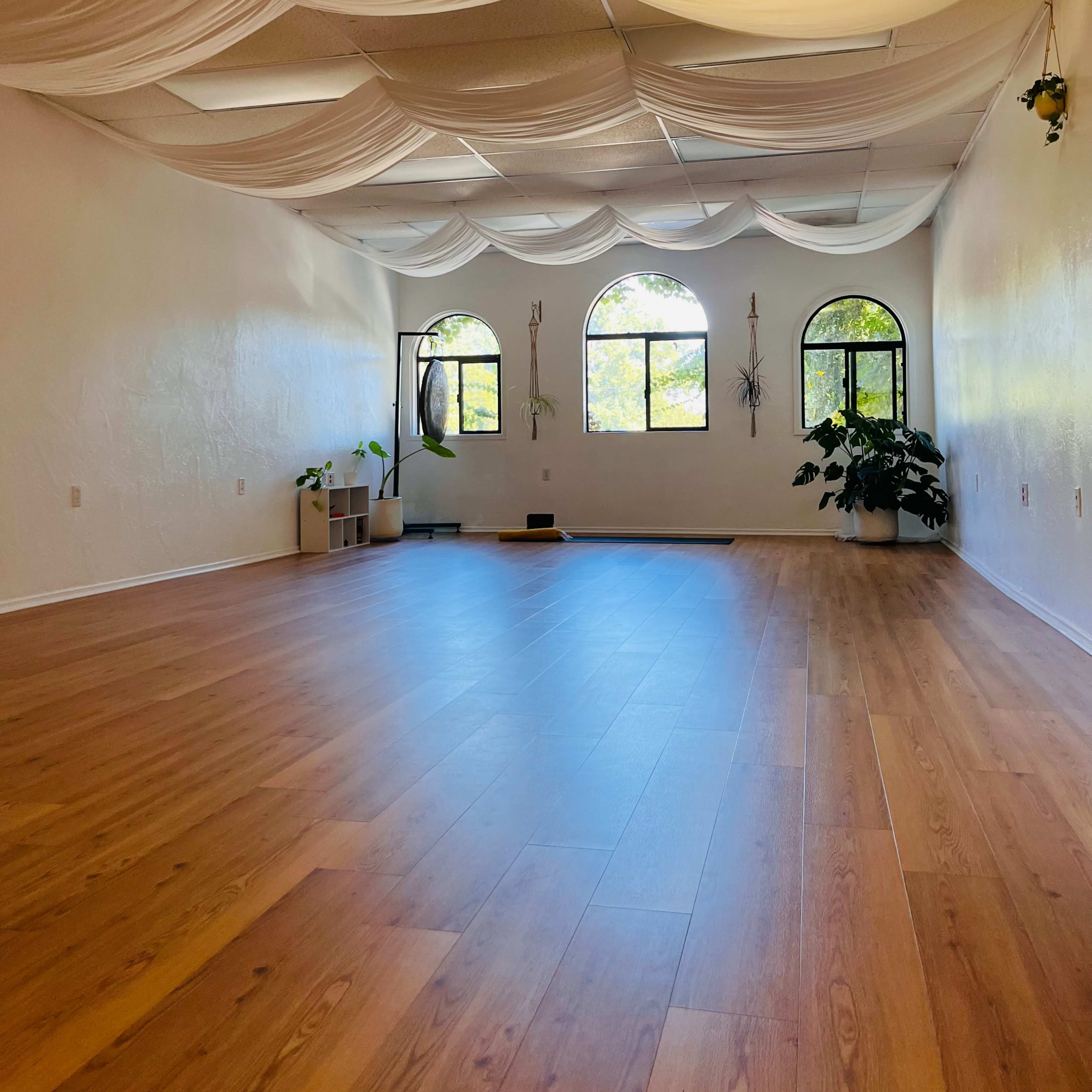 A spacious, bright room with wooden flooring, large arched windows, and draped fabric on the ceiling.