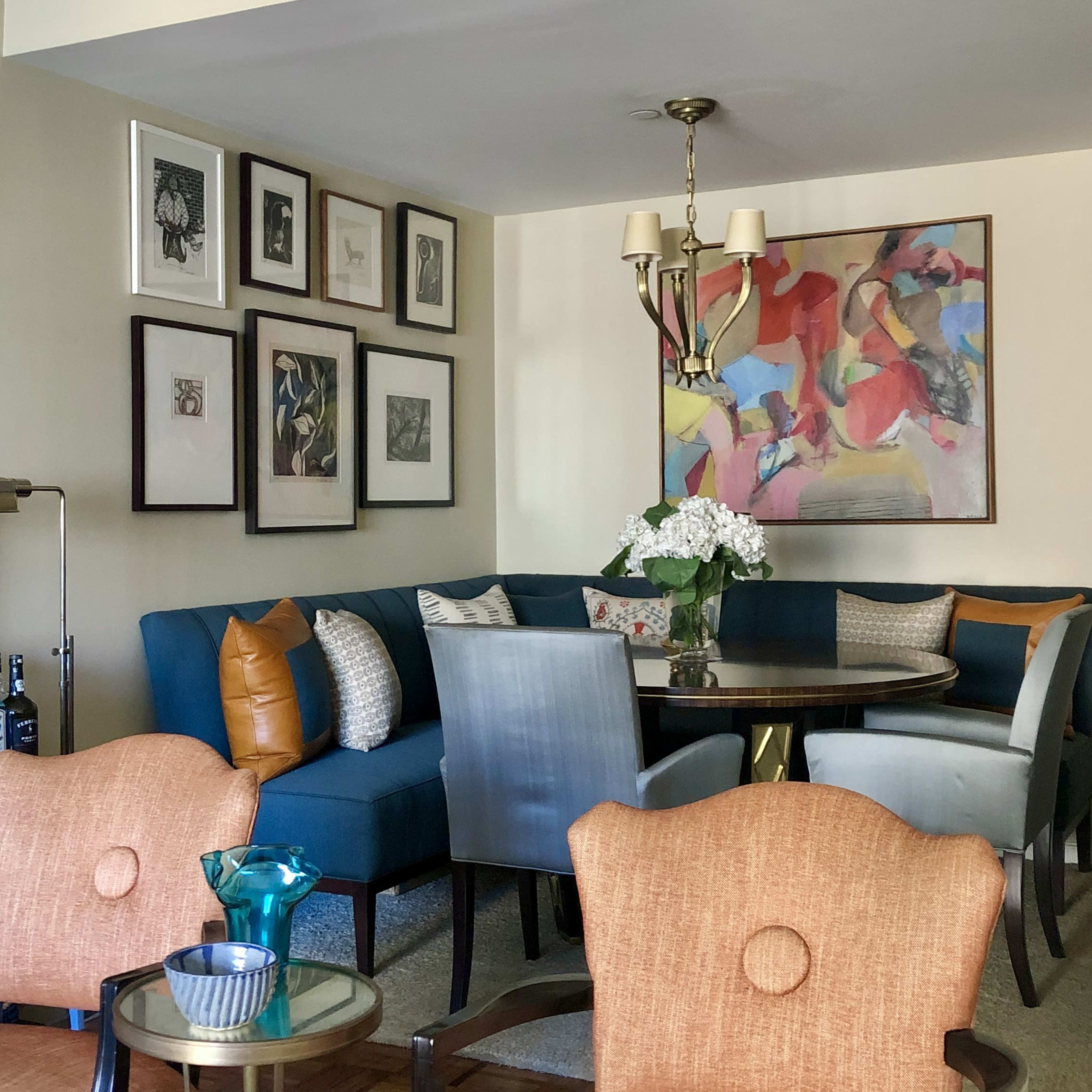 A modern living area featuring a blue sectional sofa, a round dining table surrounded by chairs, and various framed artworks on the walls.