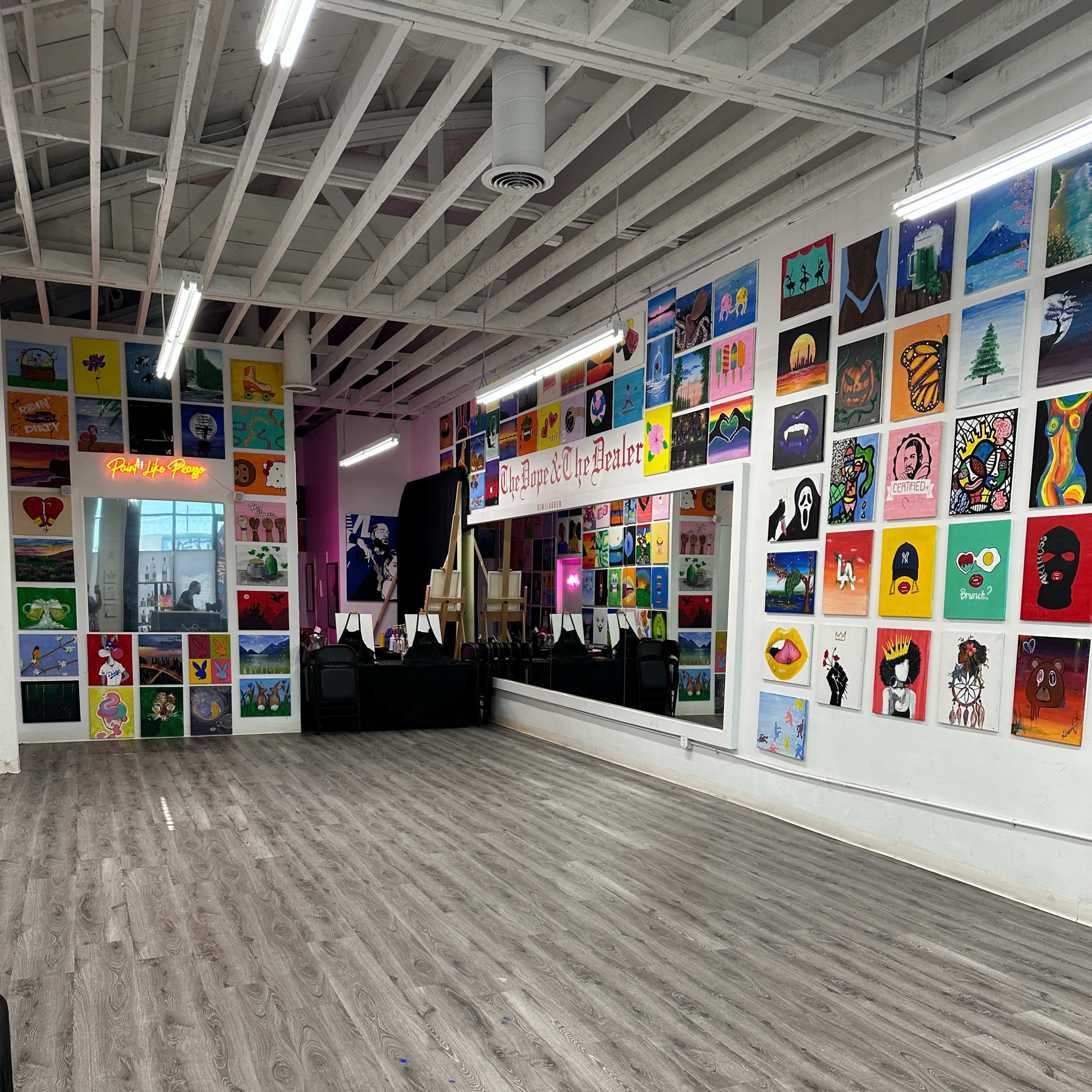 An art studio with colorful paintings displayed on the walls and a spacious wooden floor area.
