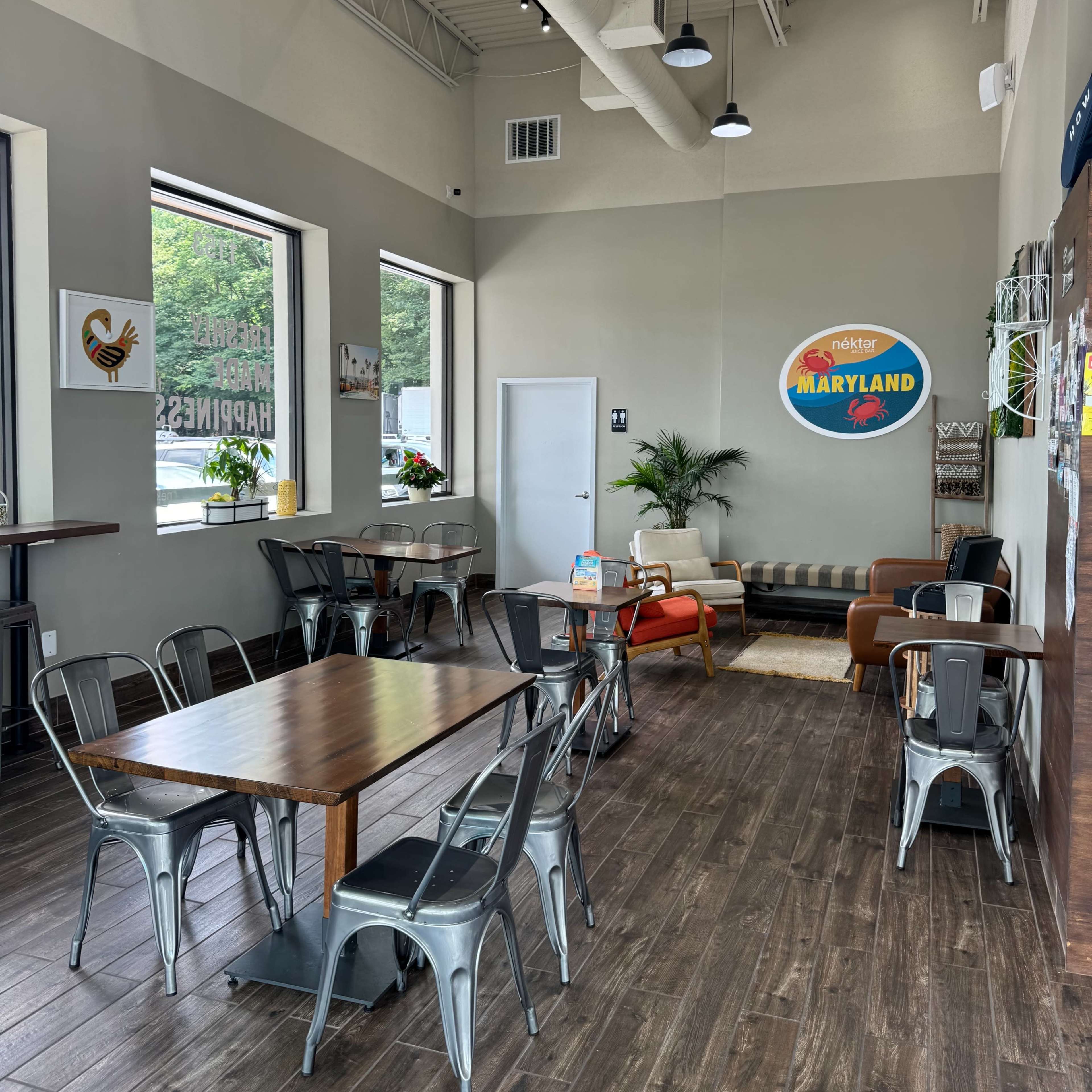 A spacious, modern café with seating options including metal chairs and wooden tables, along with a sofa and decorative wall art.