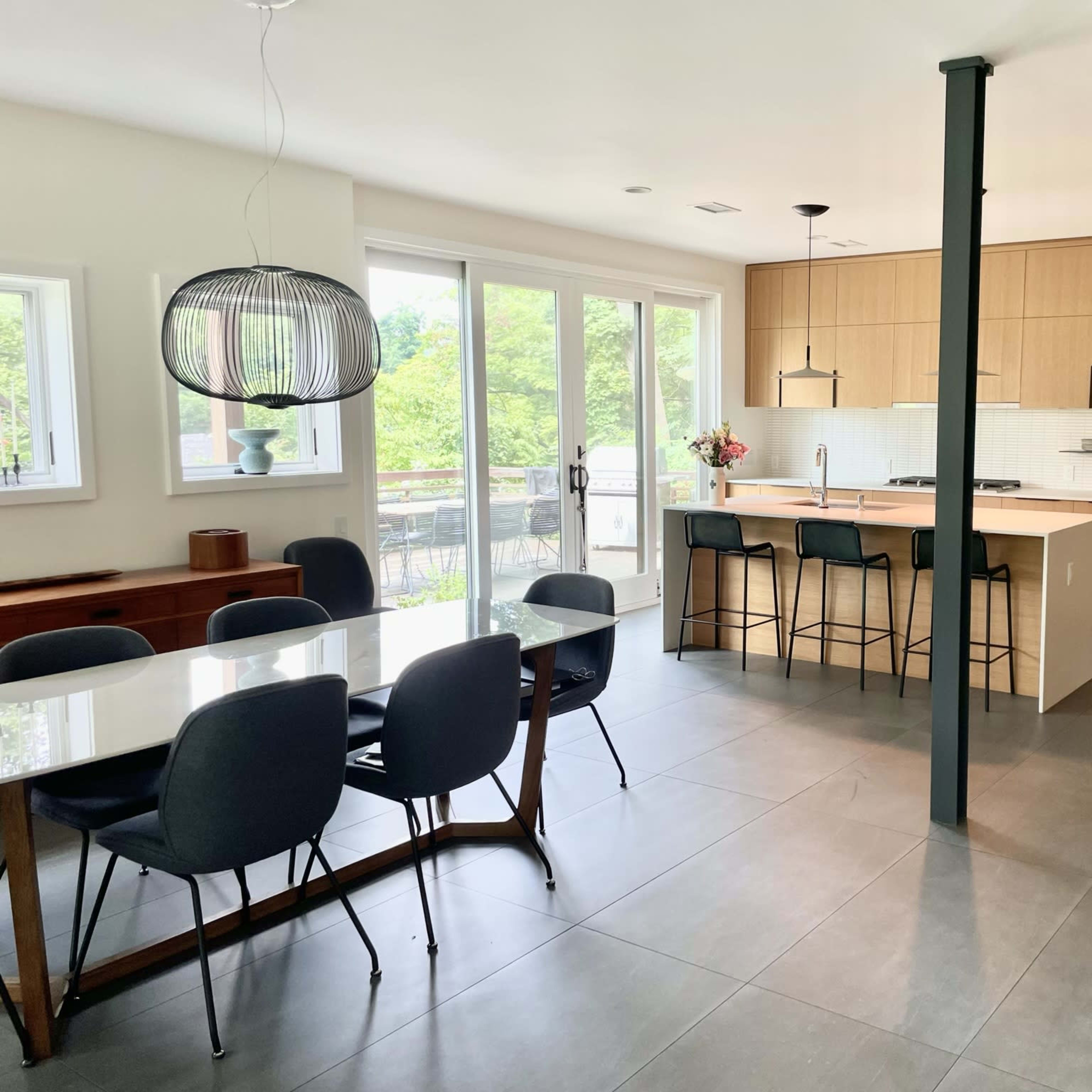 A modern kitchen and dining area features a light wood cabinetry, a large dining table, and bar stools at the kitchen counter.