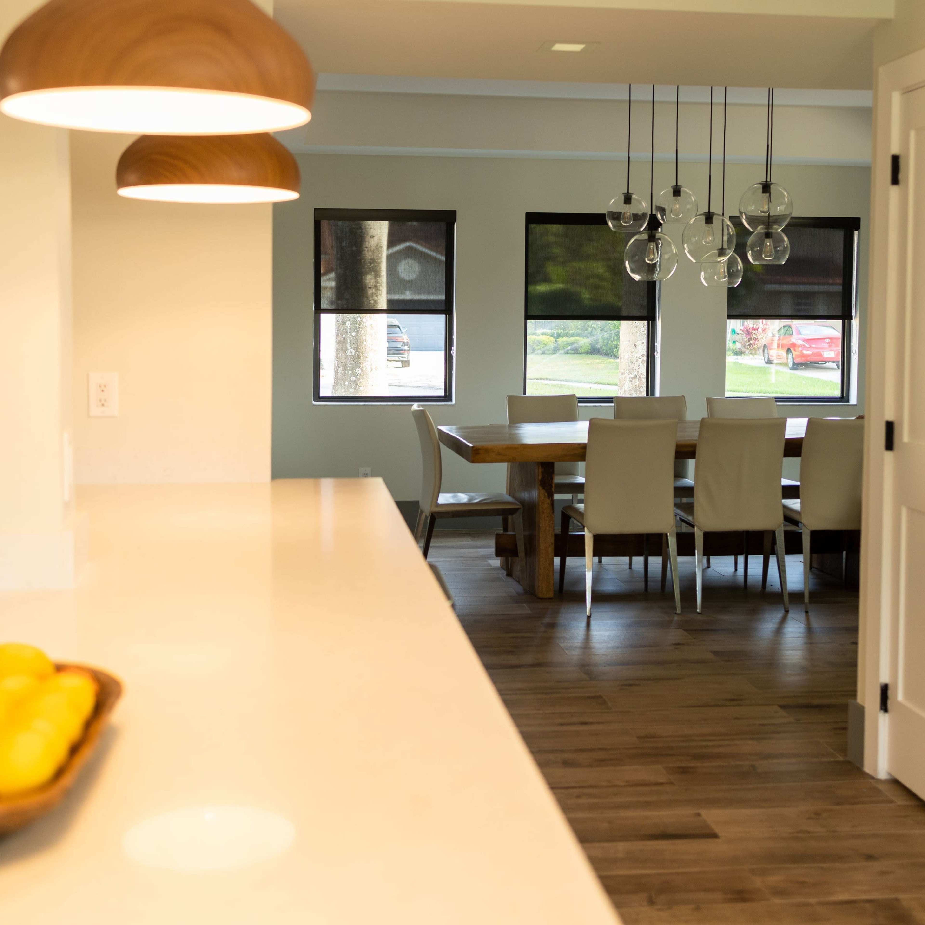 A modern kitchen features pendant lights above a countertop that overlooks a dining area with a wooden table and chairs.