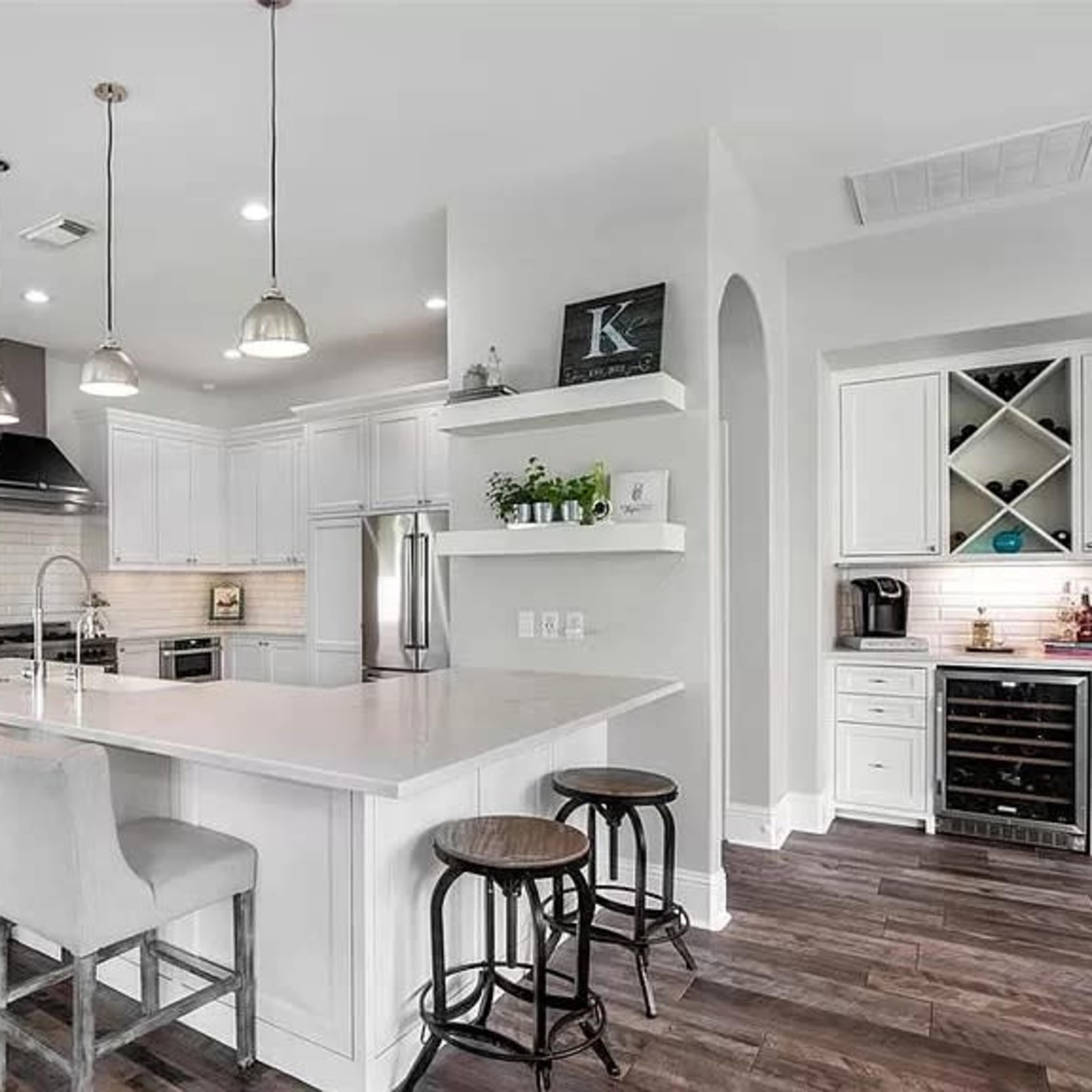A modern kitchen with white cabinetry, a large island with bar stools, and stainless steel appliances.