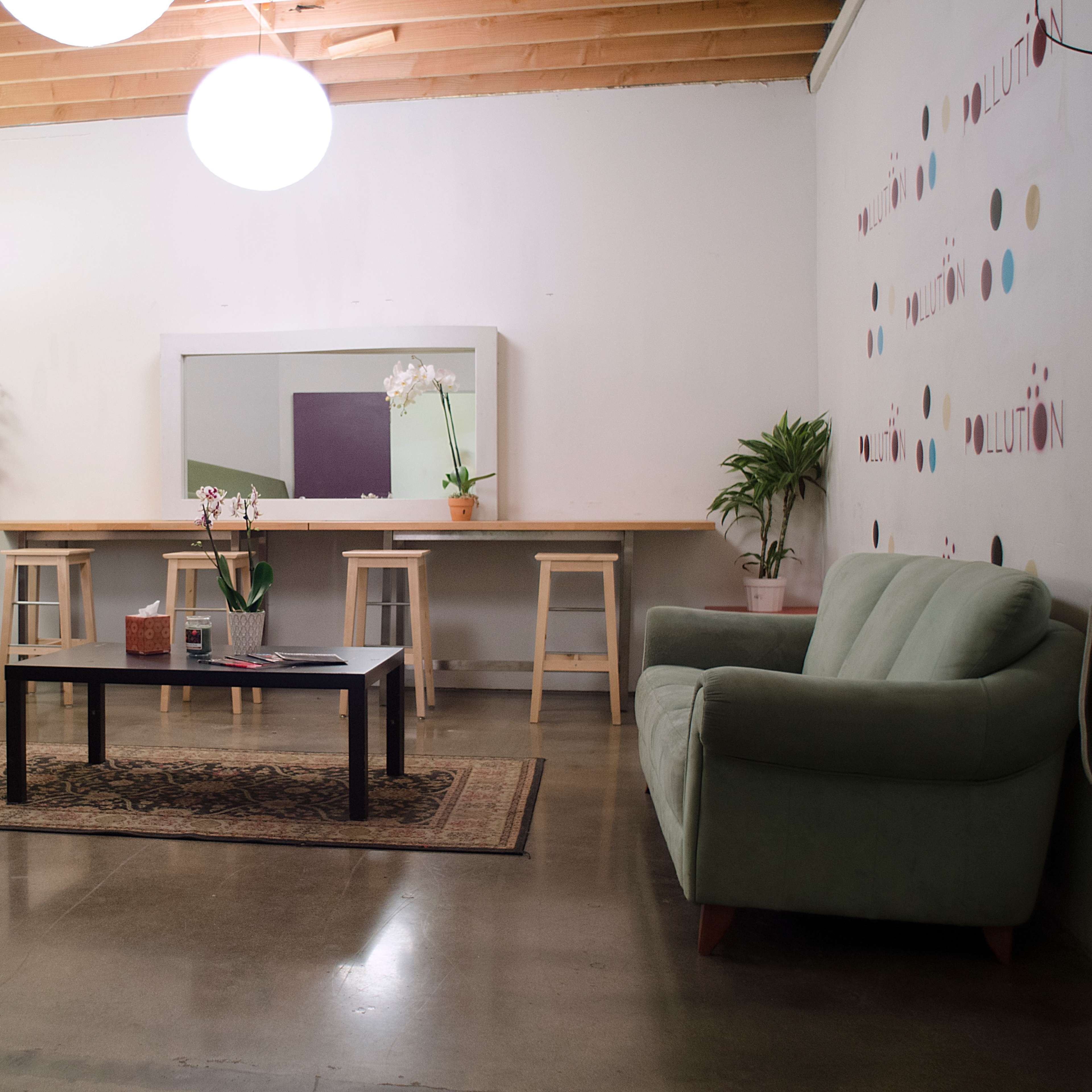 A minimalistic room features a red couch, a green couch, a rectangular coffee table, a long wooden table with stools, and a wall adorned with decorative dots.