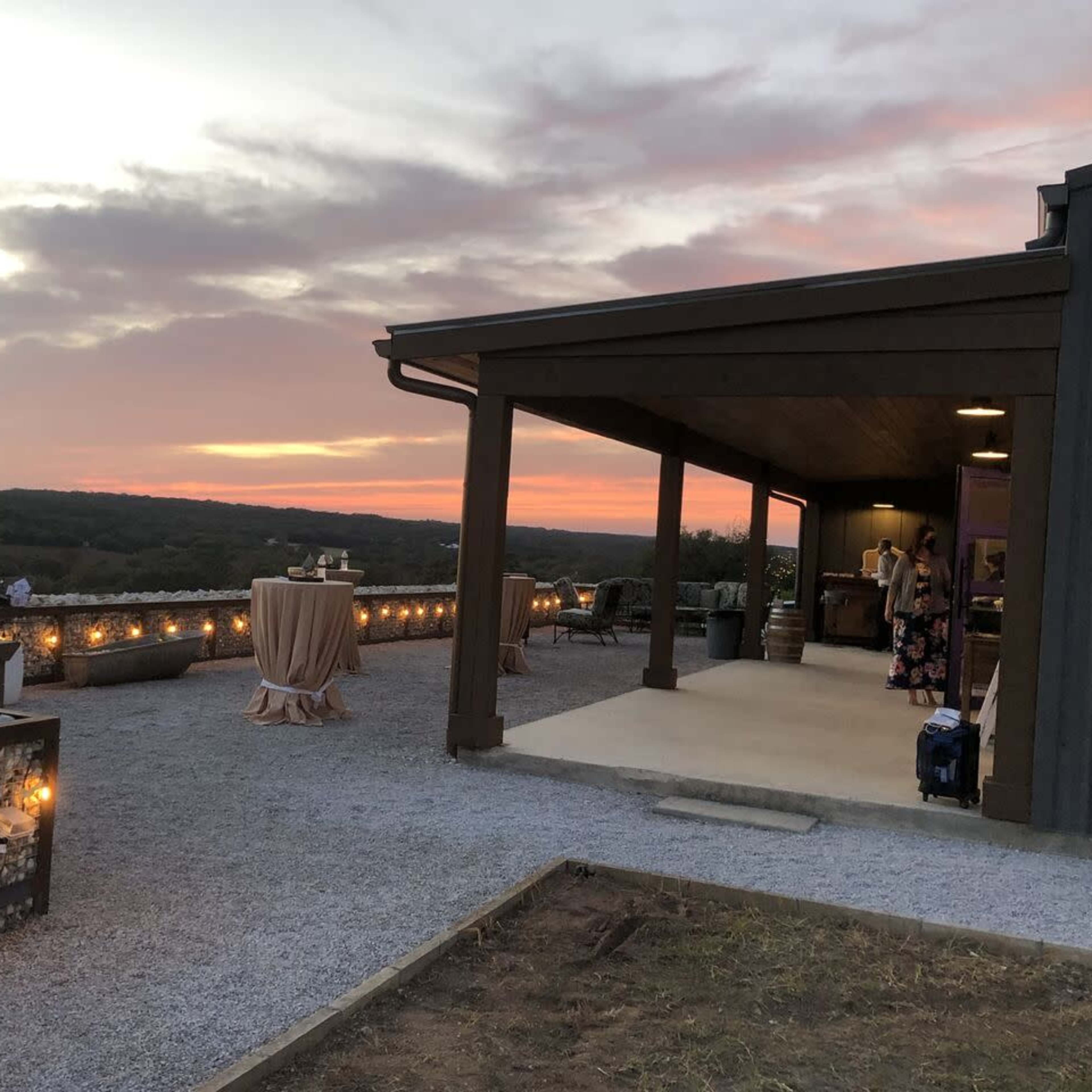 An outdoor venue at sunset with a covered area, decorative lighting, and tables set up for an event.