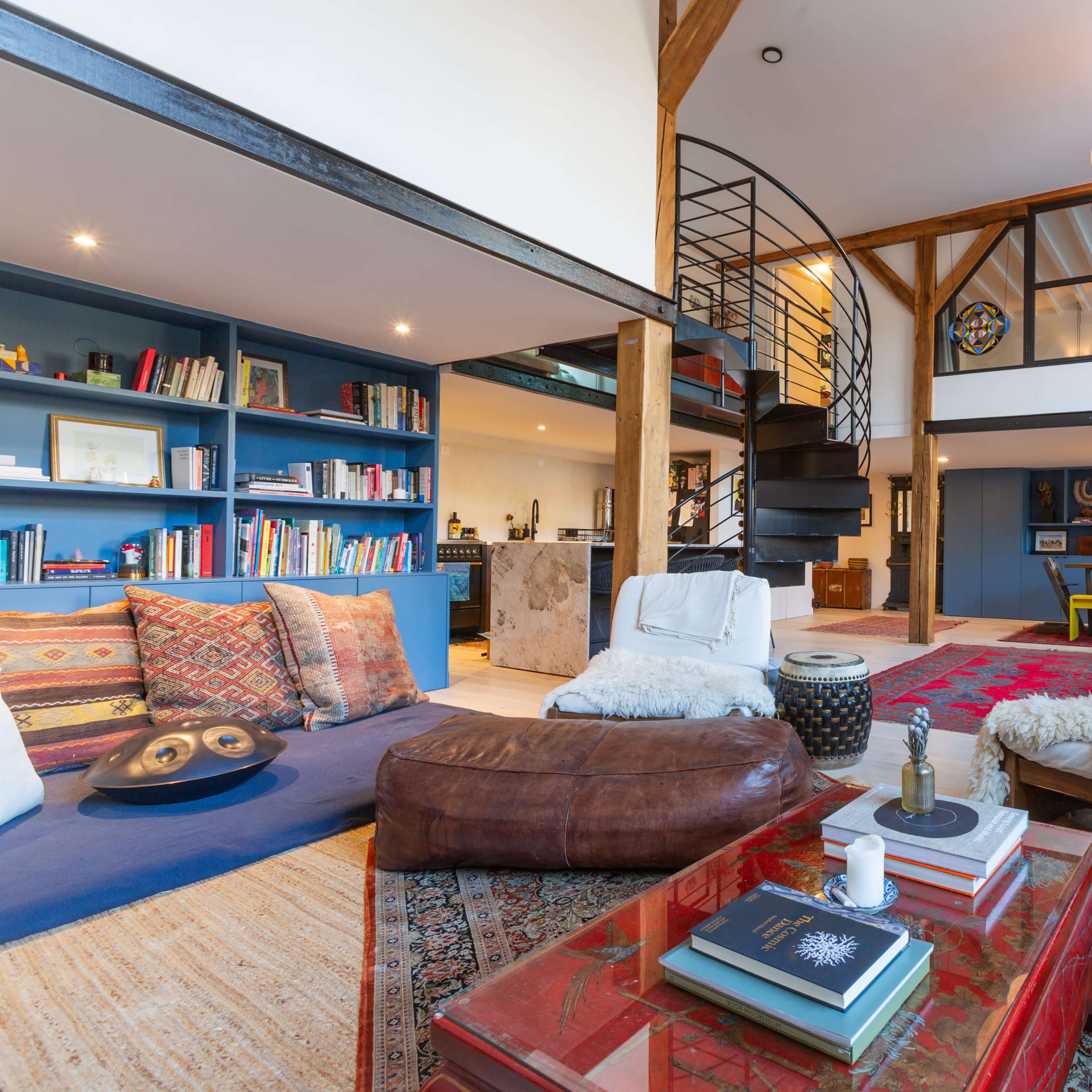 A stylish, open-concept living space featuring a spiral staircase, bookshelves filled with various books, and a seating area with a mix of cozy furniture and decorative elements.