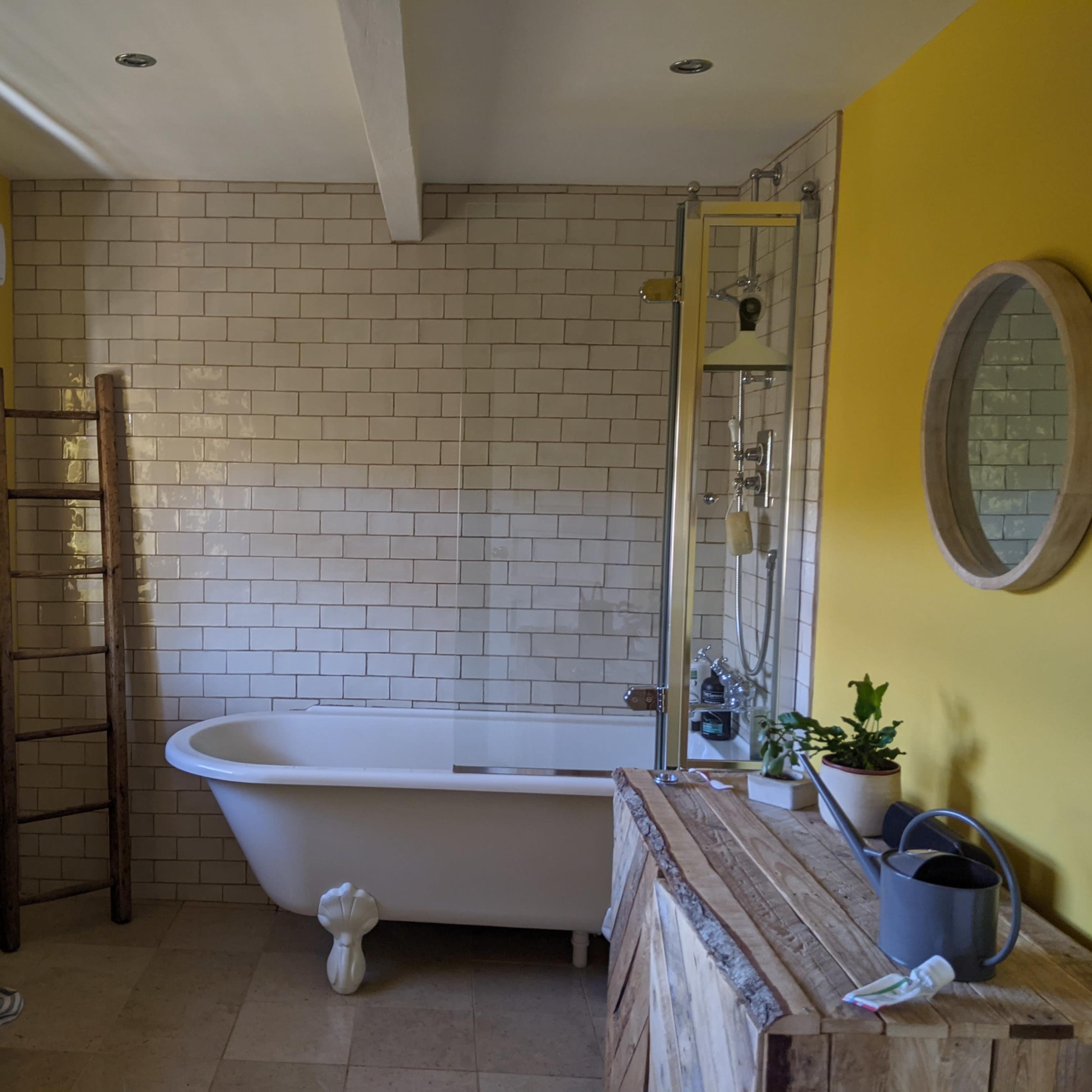 A bathroom with a freestanding bathtub, a wooden ladder, and a large mirror on a yellow wall.