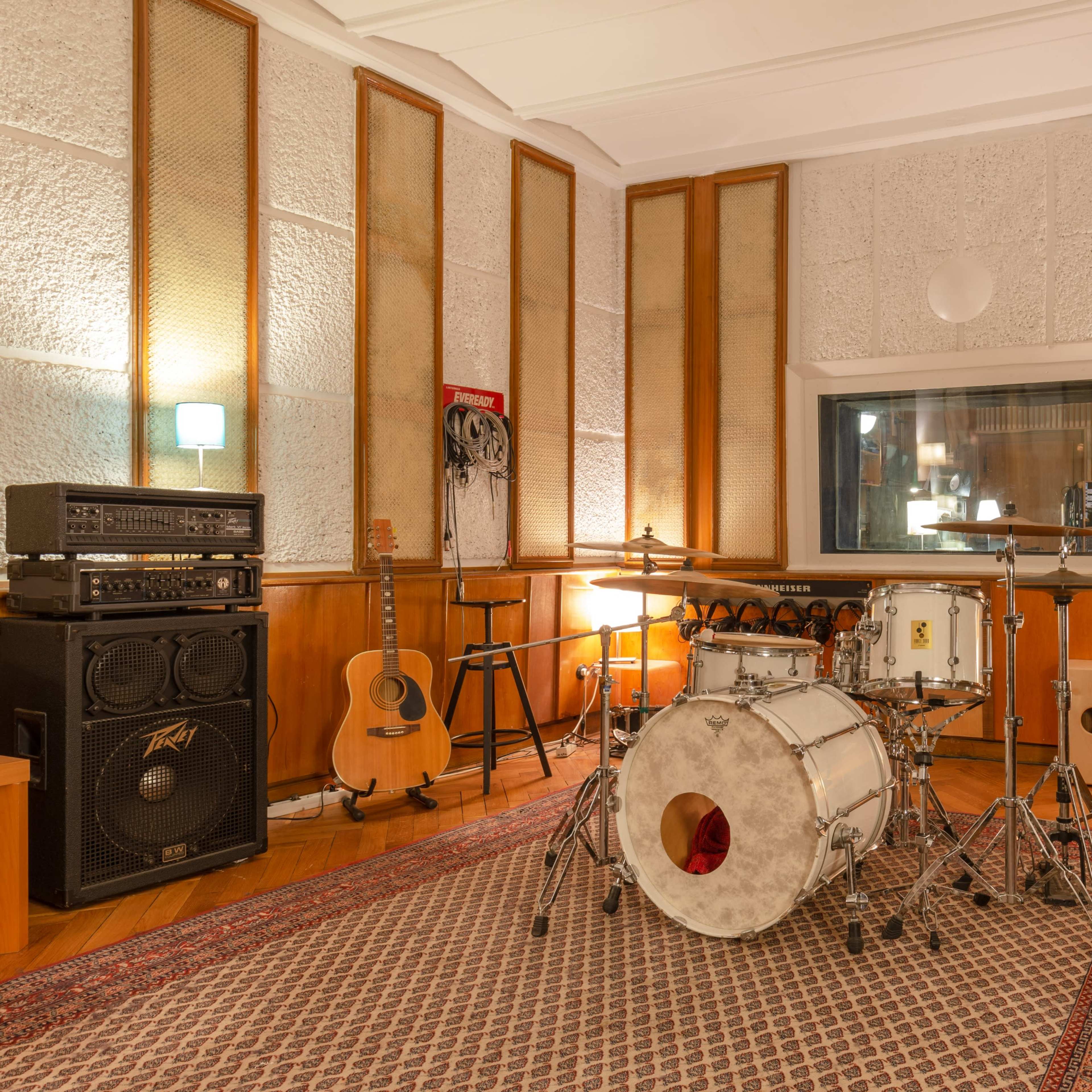A drum set is positioned in a soundproof recording studio, surrounded by acoustic panels and musical equipment.