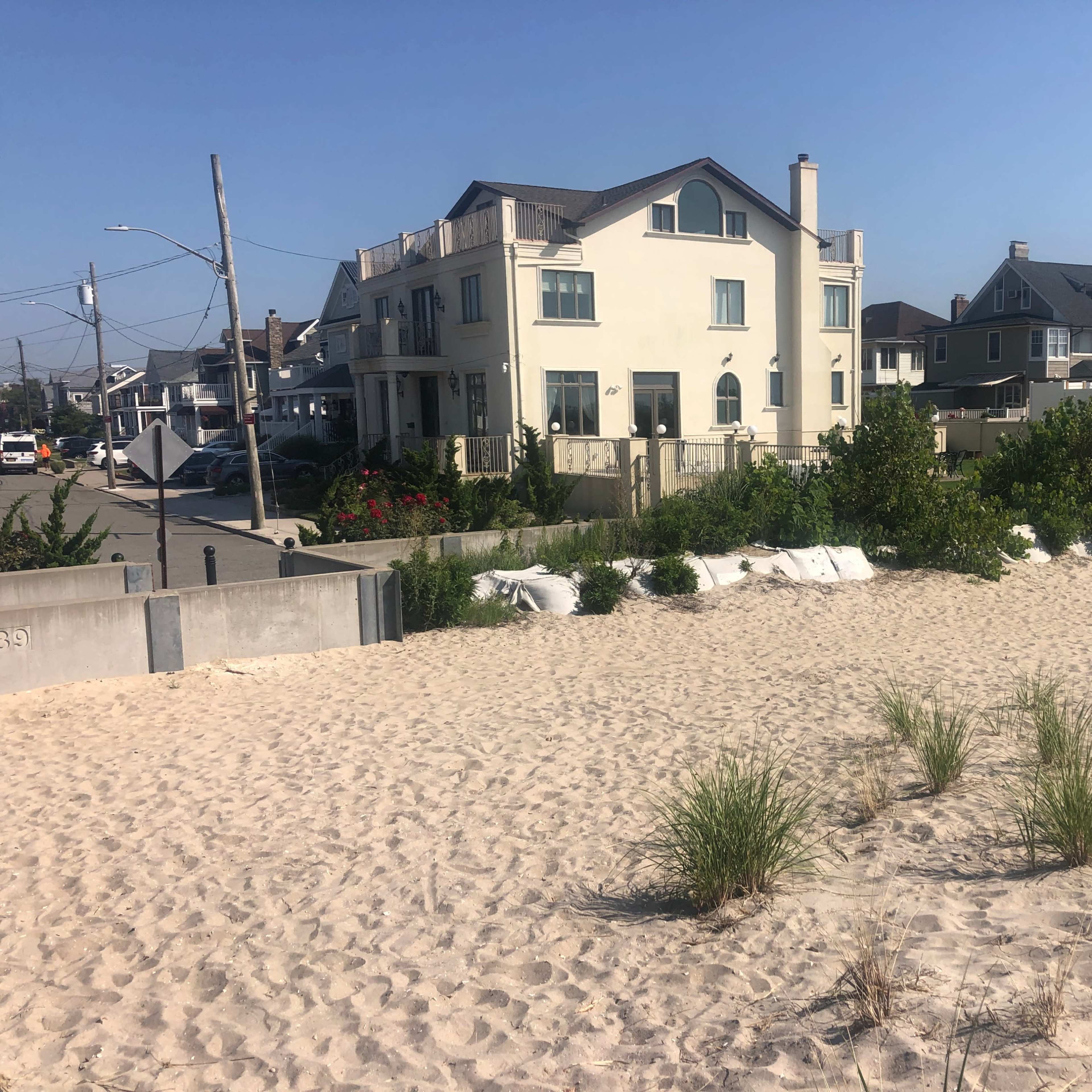 A sandy beach area with grass and a row of houses in the background.
