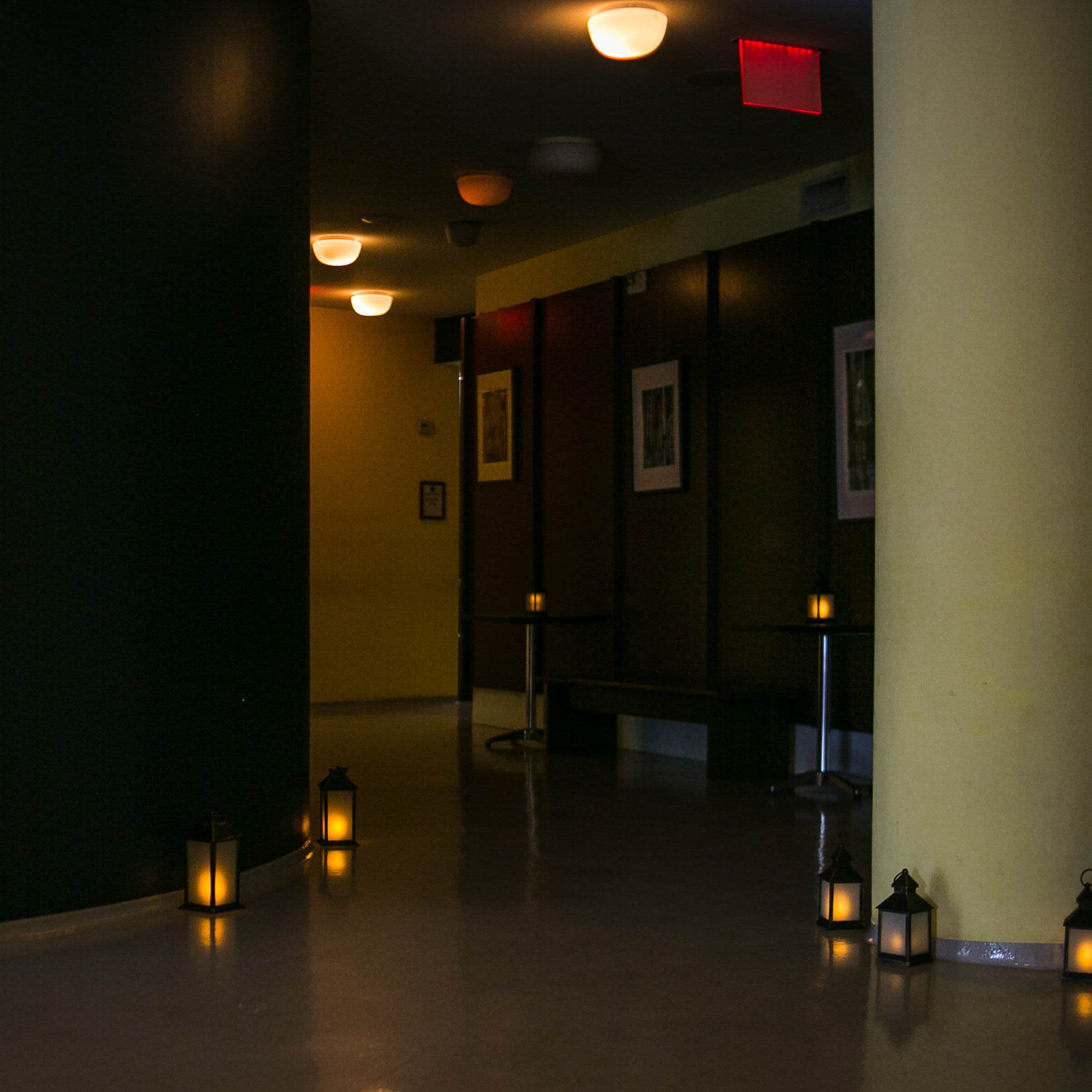 The scene features a dimly lit hallway with yellow walls and lanterns lining the floor, creating a path toward a corner.