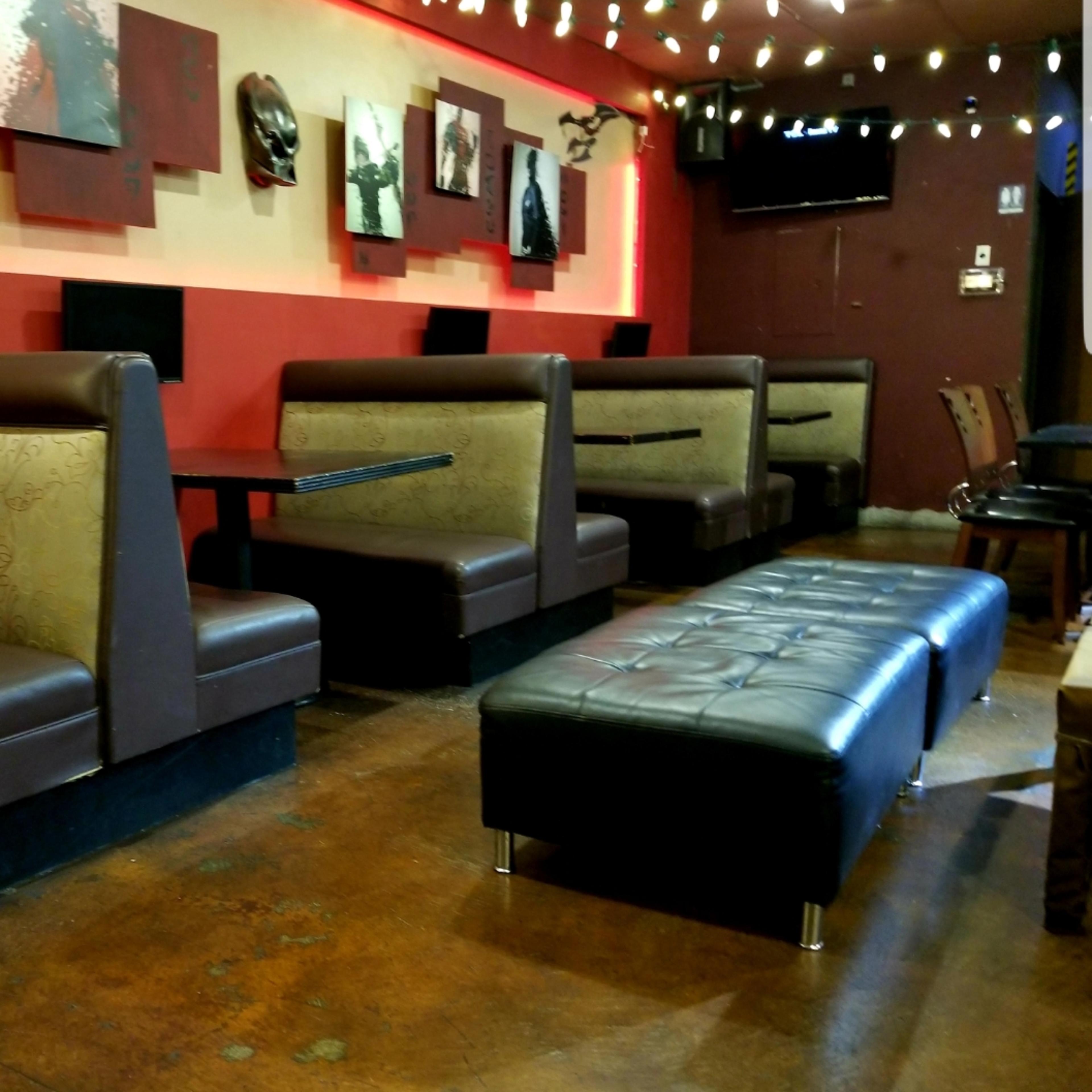 A modern café interior with several cushioned benches and tables arranged along the walls, illuminated by hanging lights.